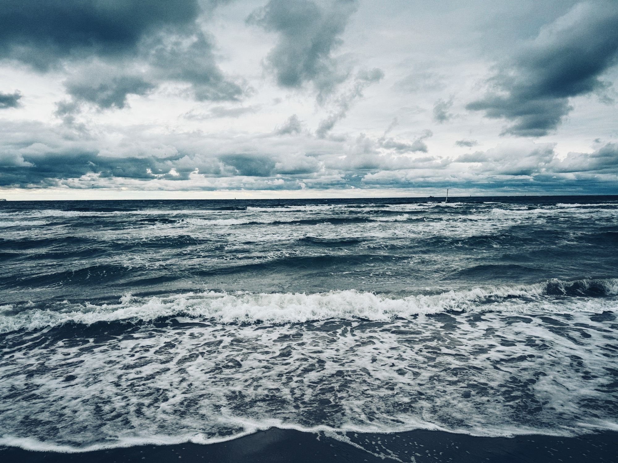 Stürmisches Wetter an der Ostsee in Warnemünde. Wellenbewegtes Wasser und ein wolkenverhangener Himmel.