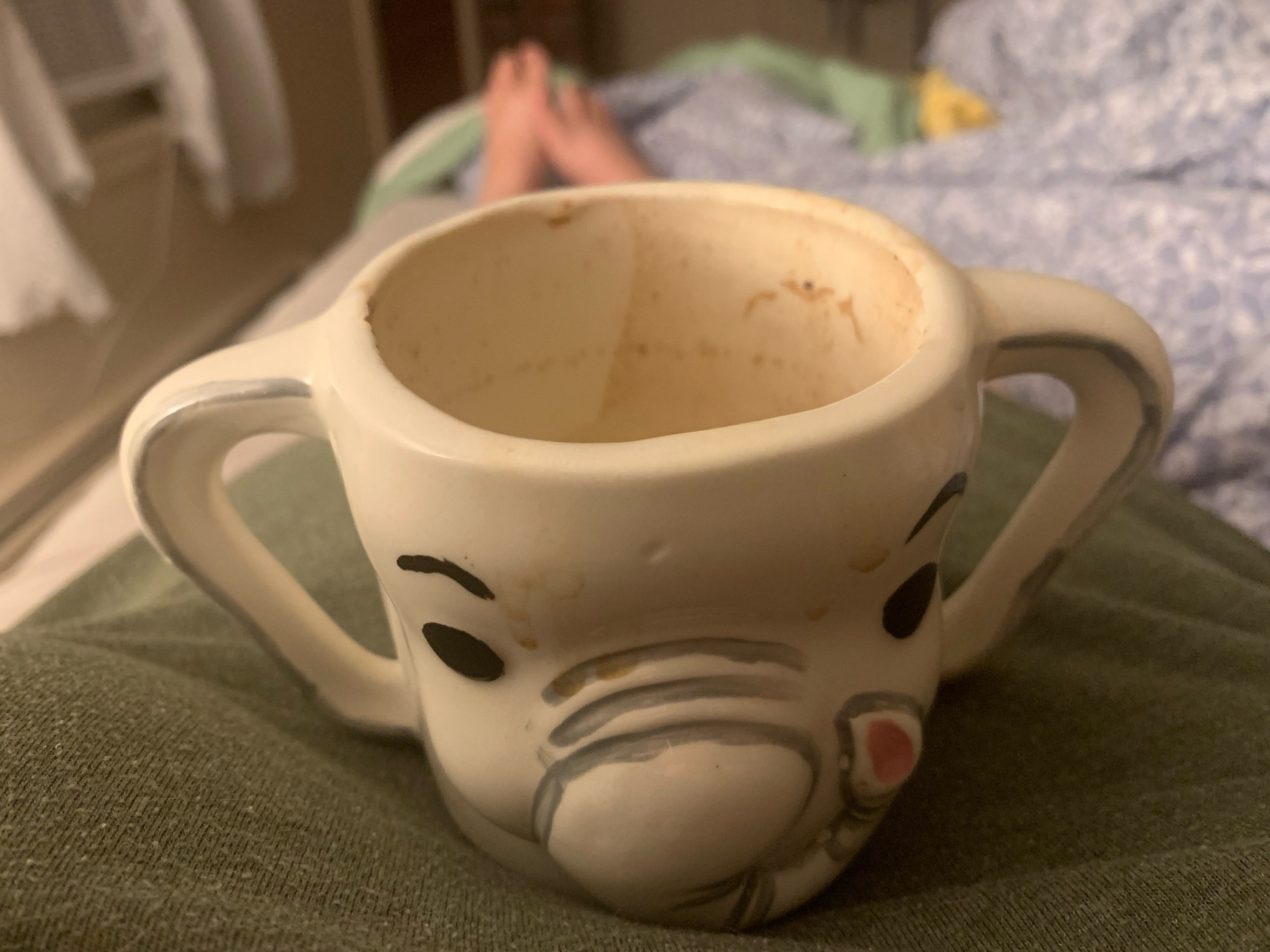 Hand painted elephant ceramic mug on a person’s chest in bed with feet in the background (fuzzed out).