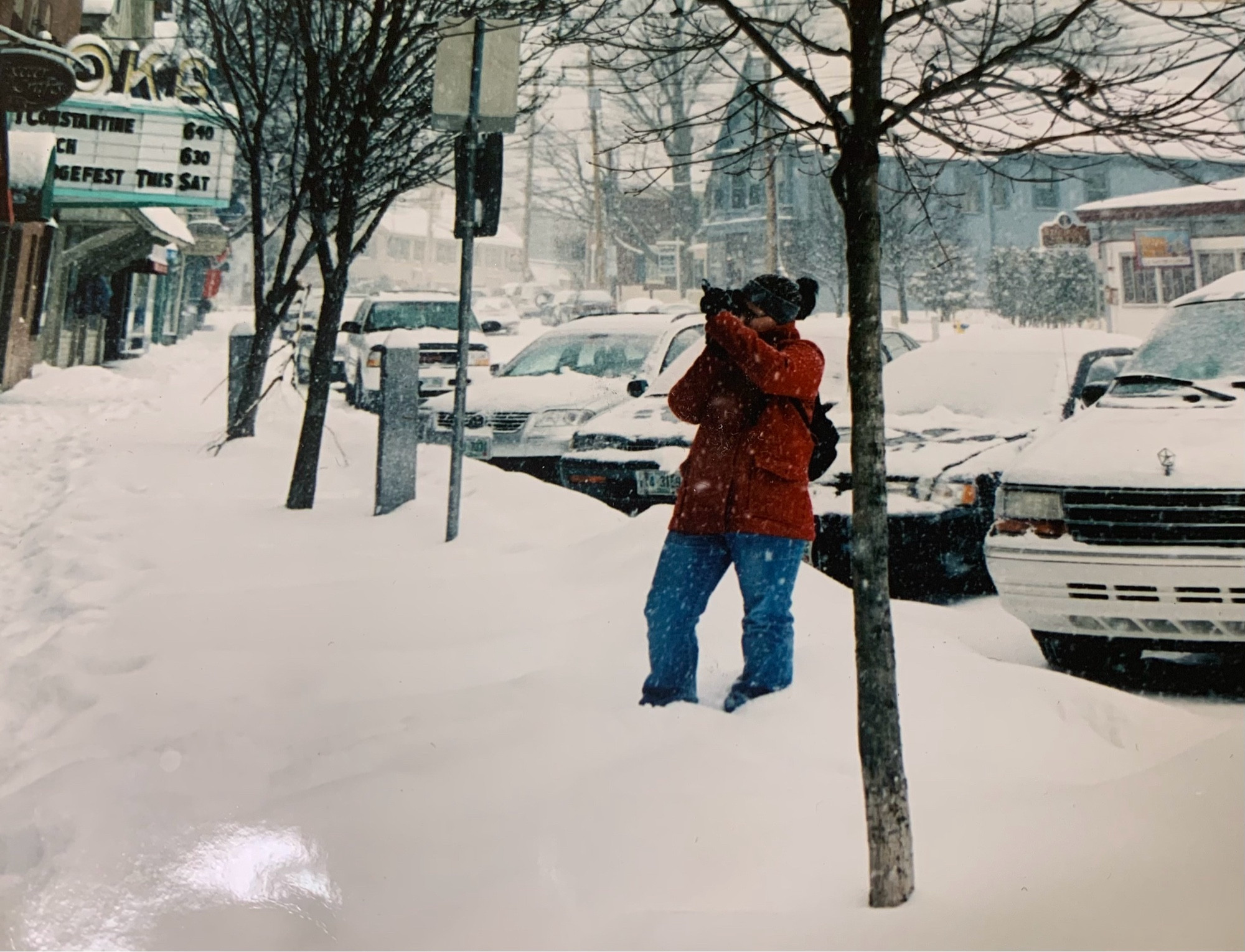 A photographer shooting in the snow in a red pea coat out front of the IOKA theatre in 2005.