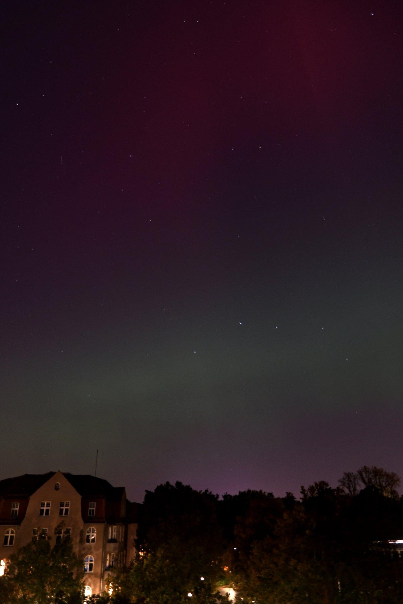 Grünes Polarlichtband am Nachthimmel über der Nachbarschaft