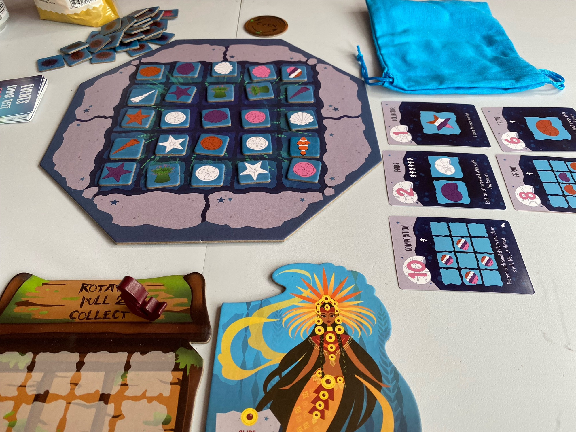 Board and cards laid out on a table for the game Moonshell. My player character looks like an Aztec princess mermaid.