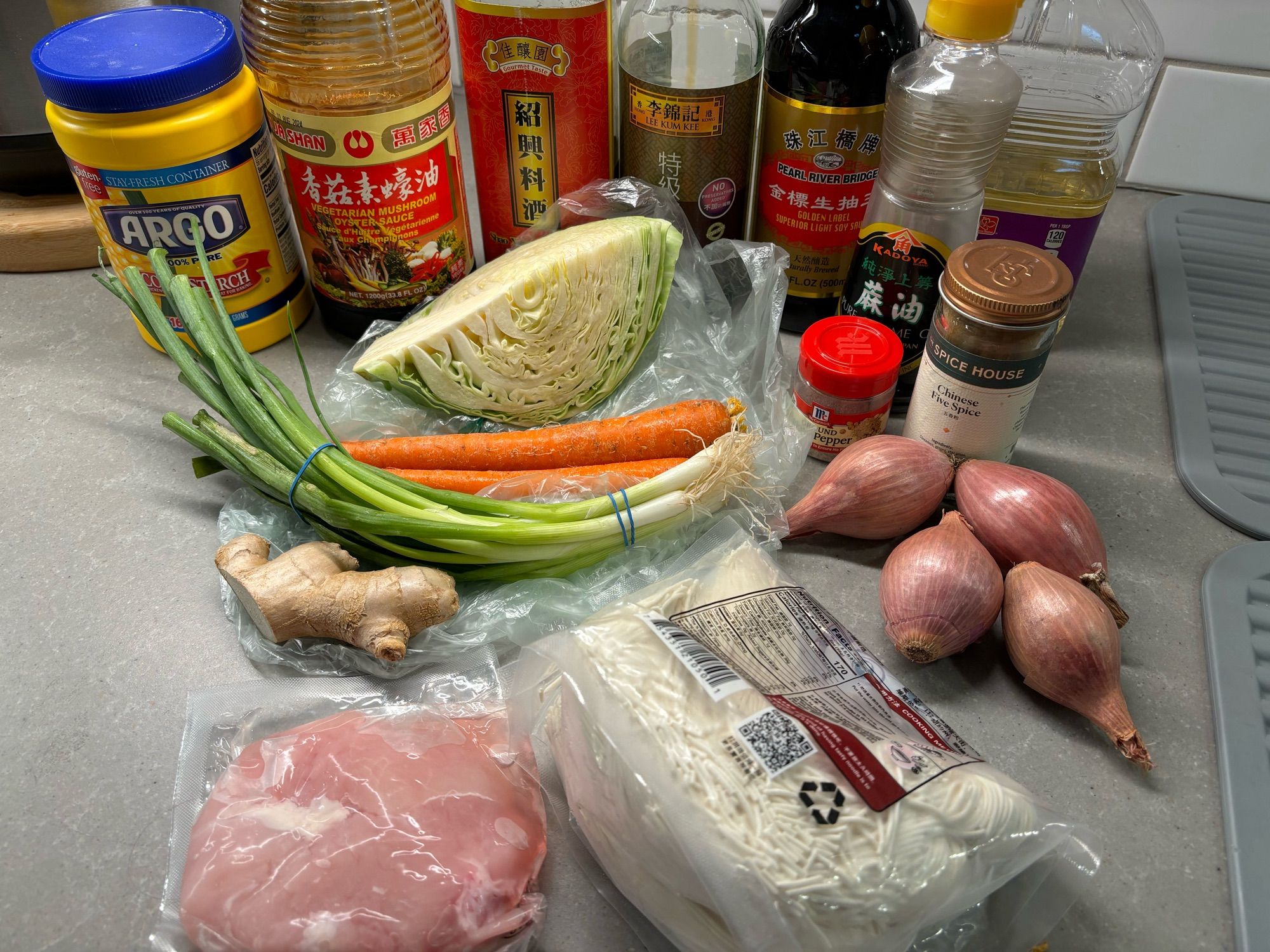 A chicken breast, noodles, cabbage, two carrots, shallots, scallions, ginger, light soy sauce, dark soy sauce, shao xing wine, oyster sauce, sesame oil, five spice and white pepper on a kitchen counter