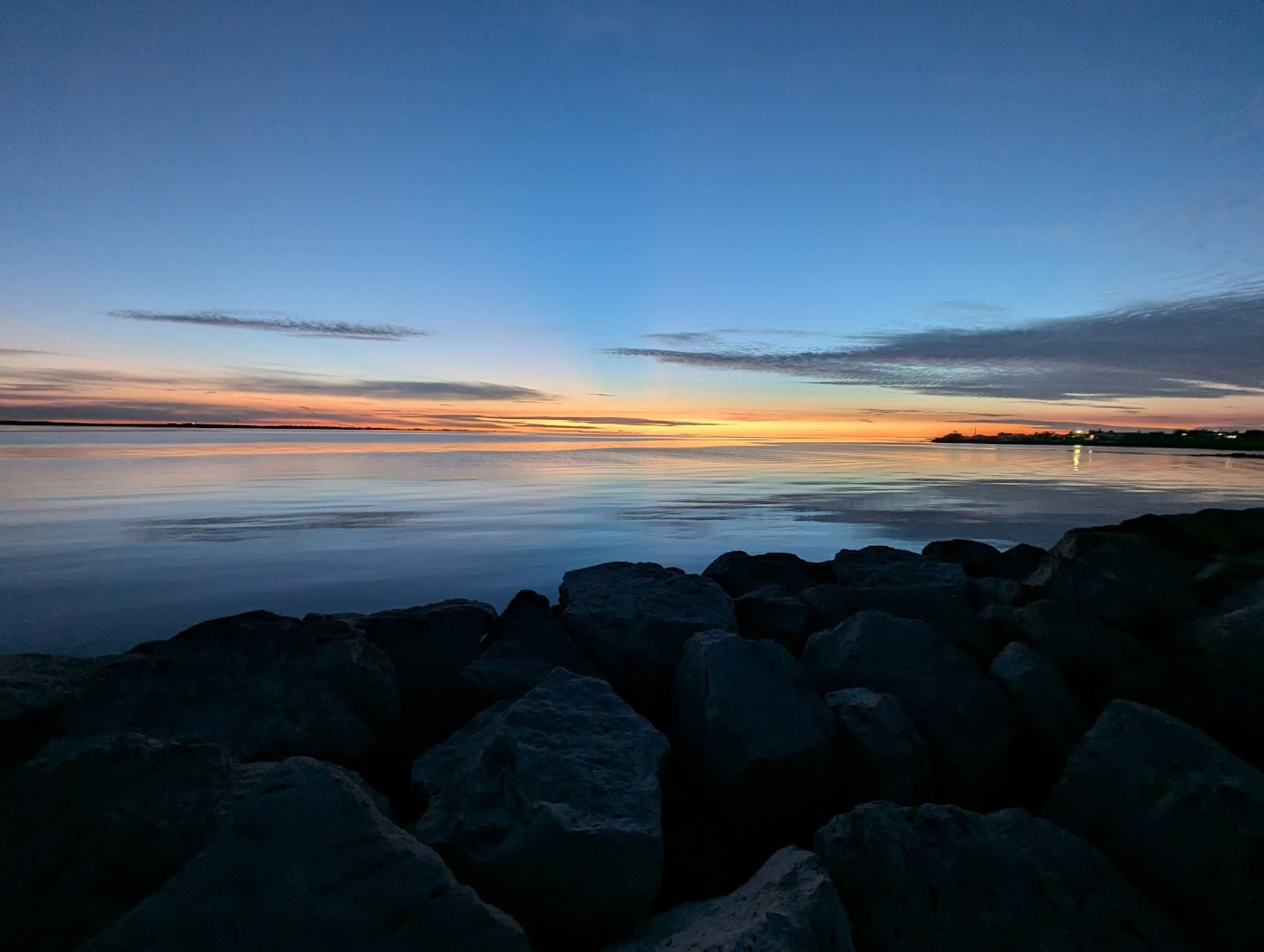 Horft á sólsetur nærri Nauthólsvík, sjórinn er sléttur.