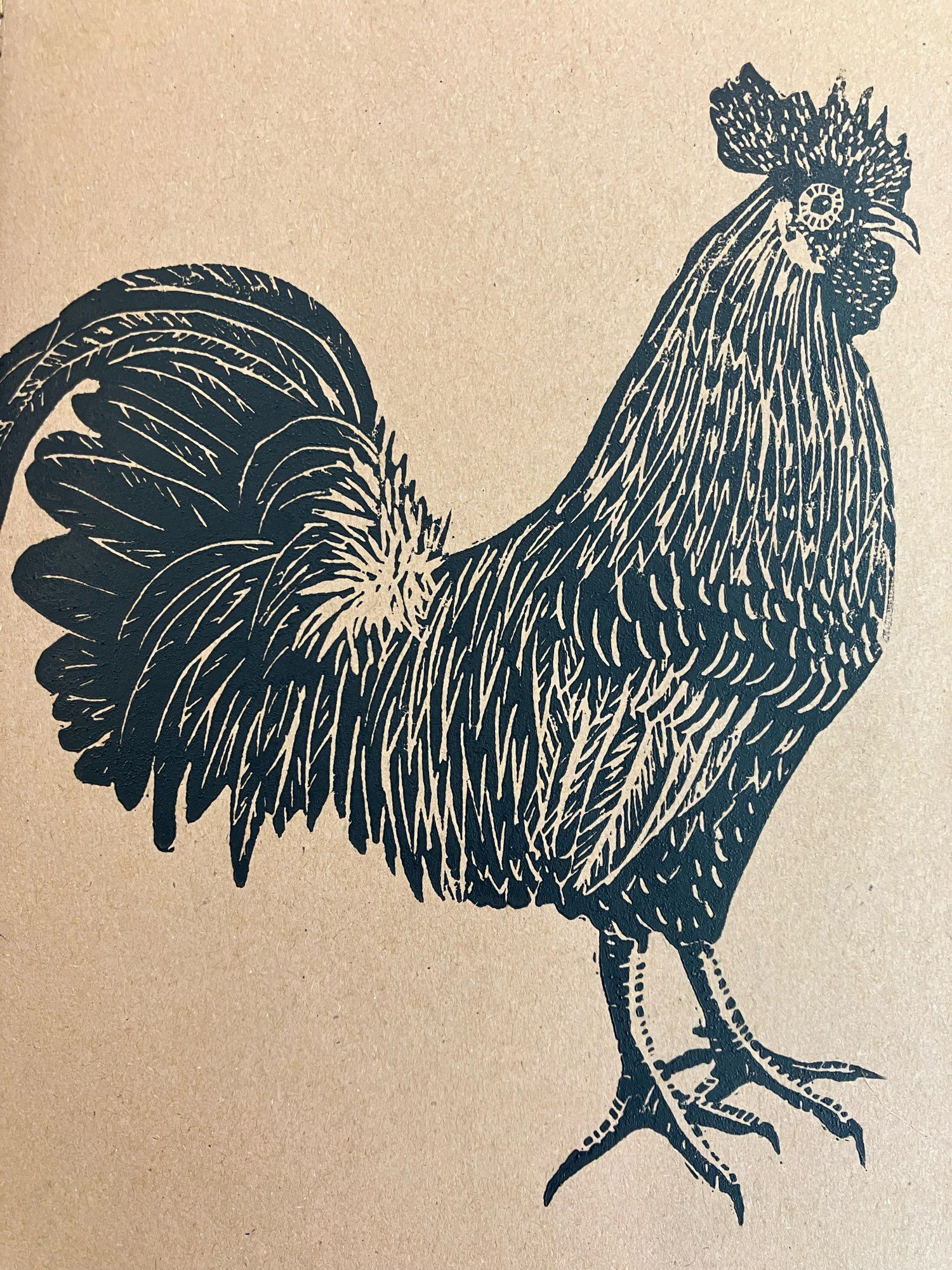 Linoleum blockprint of a rooster in black ink on brown Kraft paper