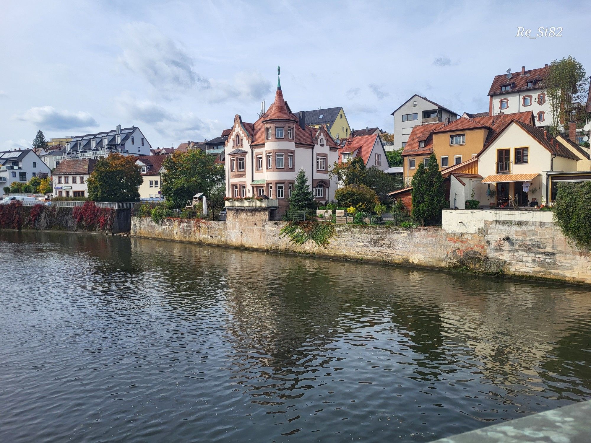 Im Vordergrund ein Fluss, begrenzt von einer Mauer, dahinter Wohn- und Geschäftsräumen mit max. 3 Stockwerken. 