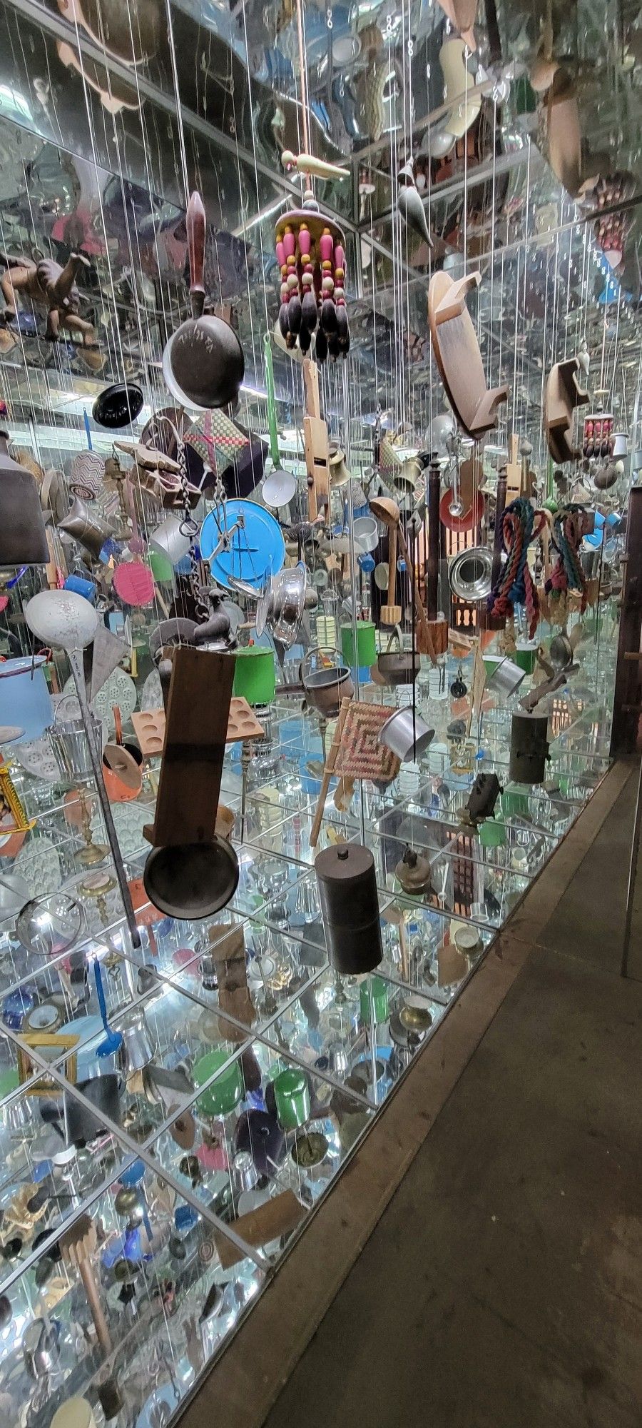 Household items hung in front of a wall of mirror tiles. Art installation.