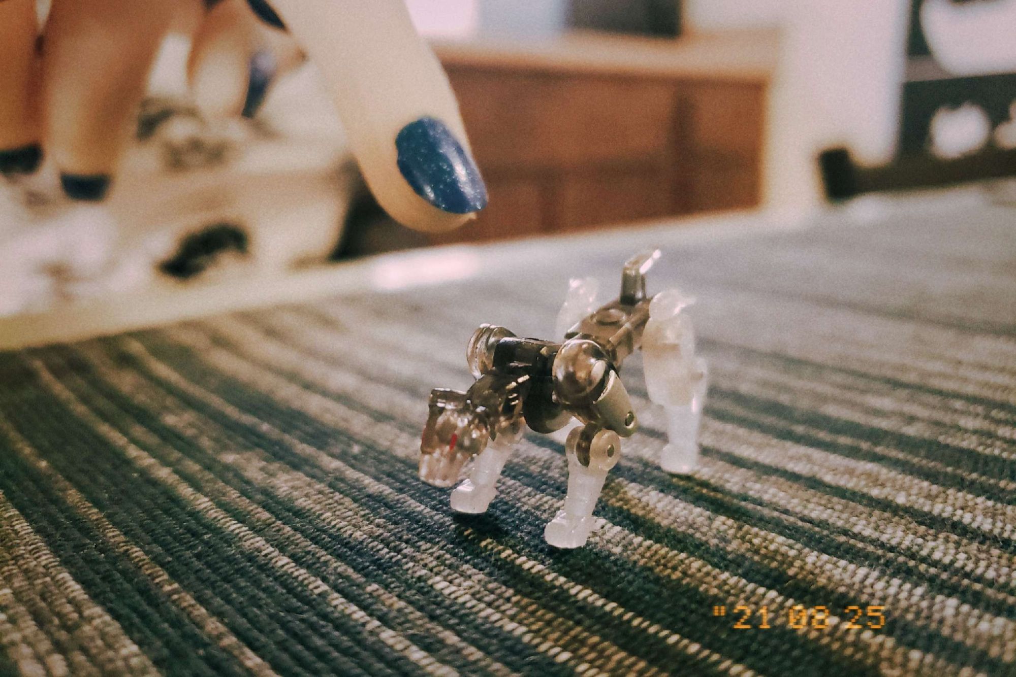 A photo of the exceptionally small Ravage figure that came with the tiny Soundwave seen in the previous photo, standing on a placemat that looks like black-and-white television scan lines. He's in mechanical panther mode, and like Soundwave, is translucent. Miss Winter's rubbery index finger is at the photo's top left, helpfully pointing out teeny tiny Ravage.