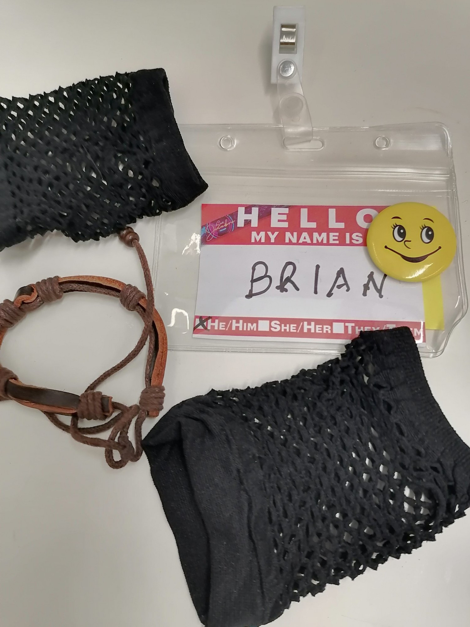 Una tarjeta de identificación de "Brian", una chapa de Smiley, una pulsera de cuero y unos guantes negros de rejilla