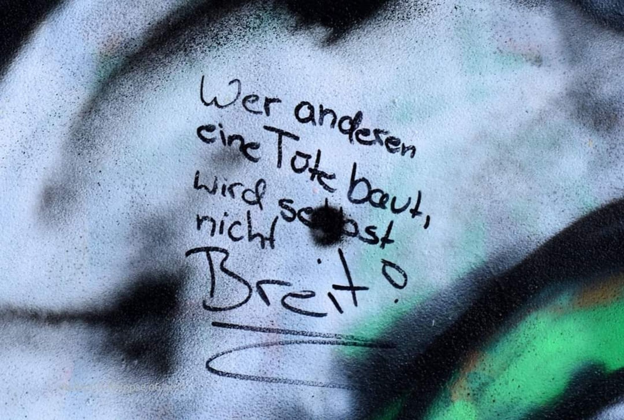 Auf bunt angesprühtem Untergrund steht in schwarz geschrieben: "Wer anderen elne Tüte baut, wird selbst nicht Breit!"