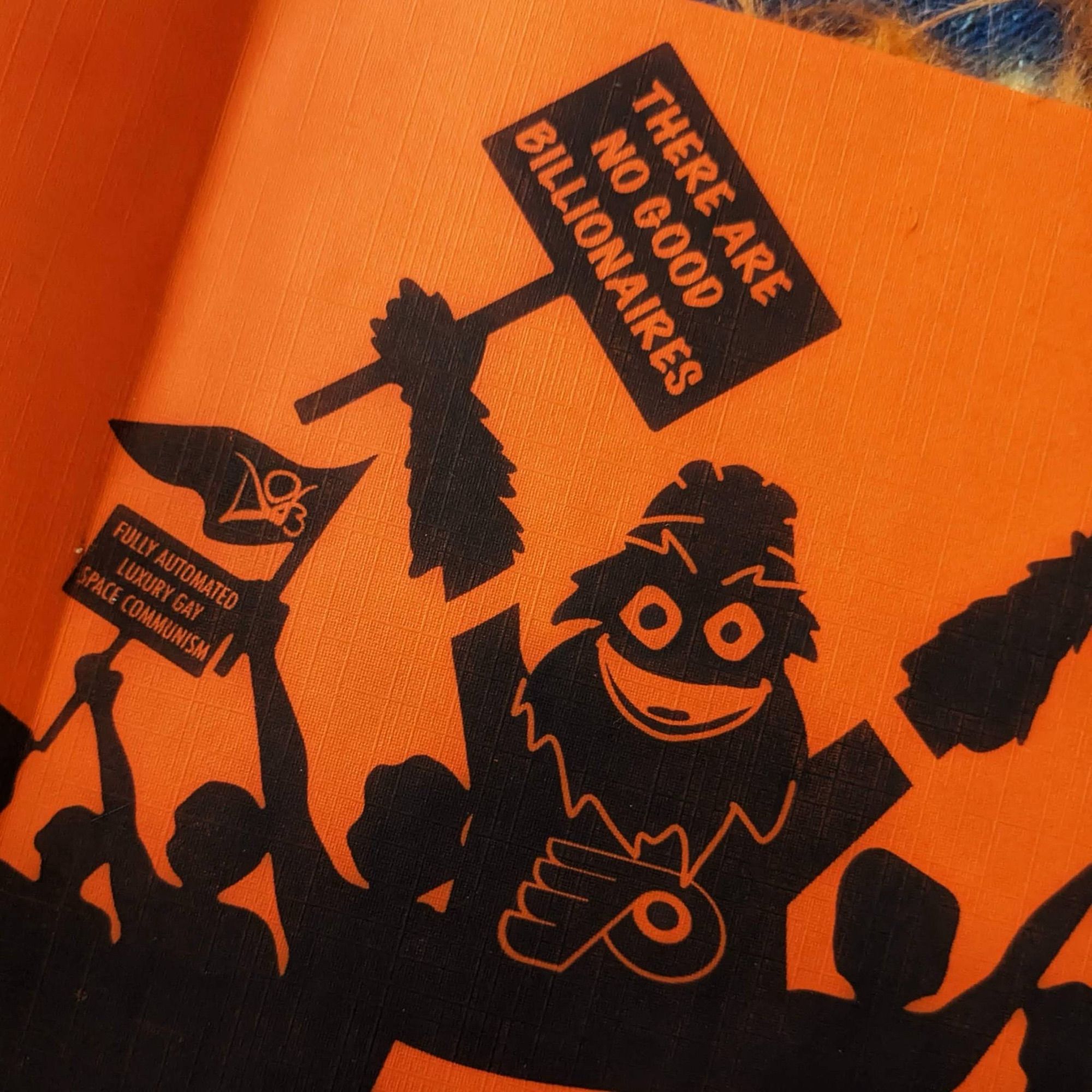 The glorious endpapers of this glorious book feature black silhouettes on an orange background of people holding up anticapitalist signs, including Gritty whose sign says “There are no good billionaires”