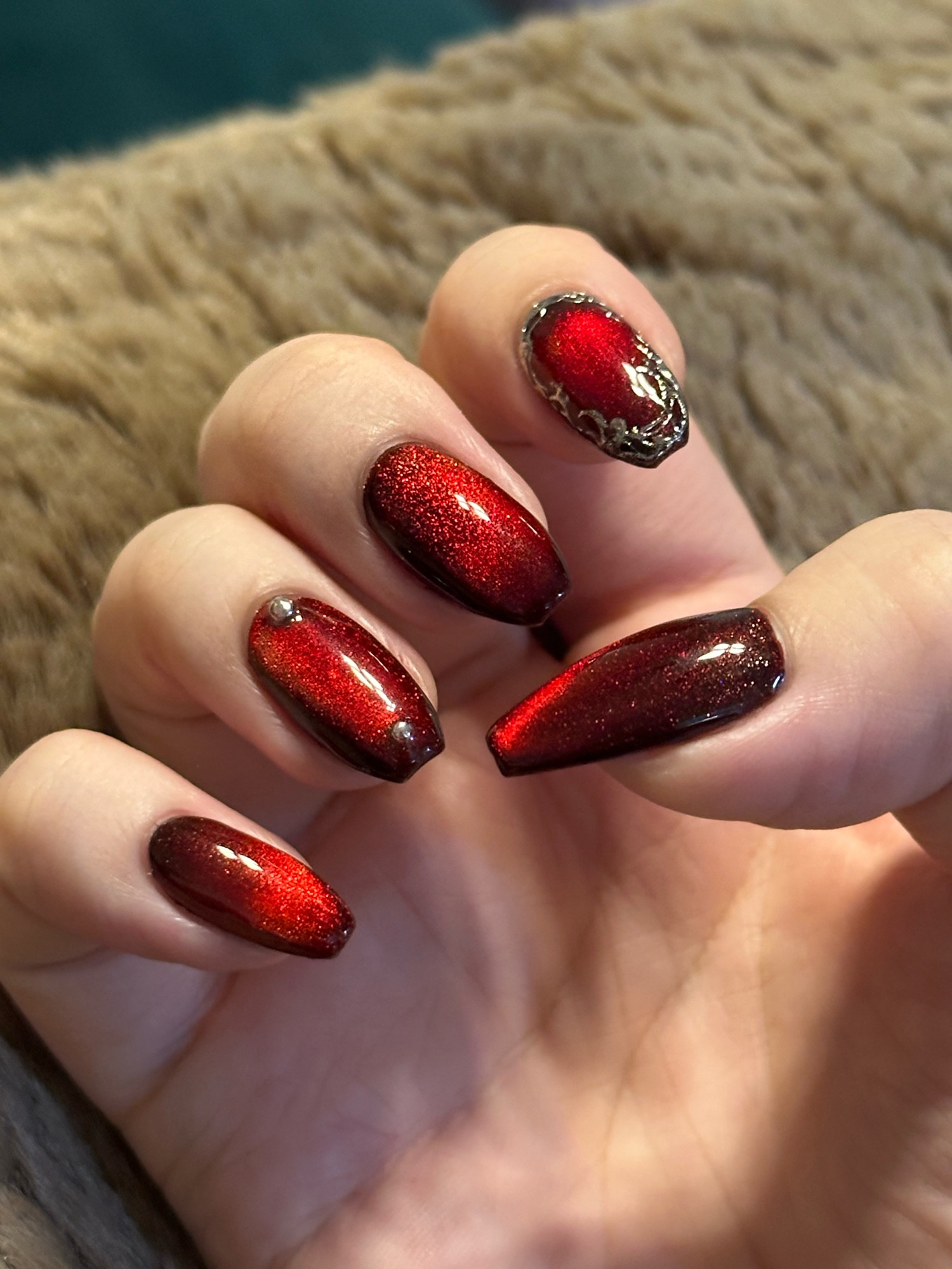 Red nails with a sparkly magnetic effect and silver nail art. 