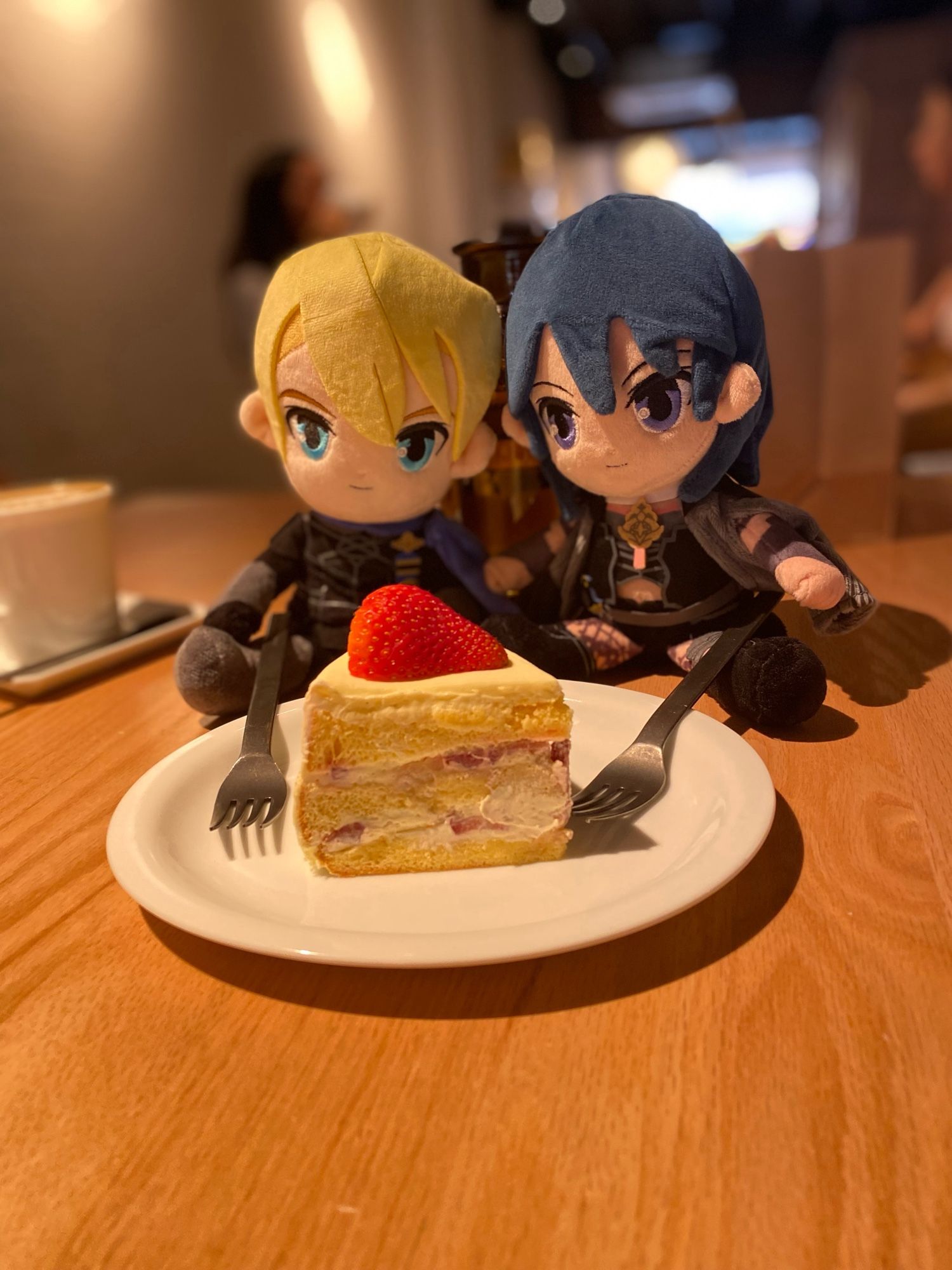 Plush toys of Dimitri and Byleth from Fire Emblem Three Houses posed behind a slice of strawberry chiffon cake as though sharing it on a date