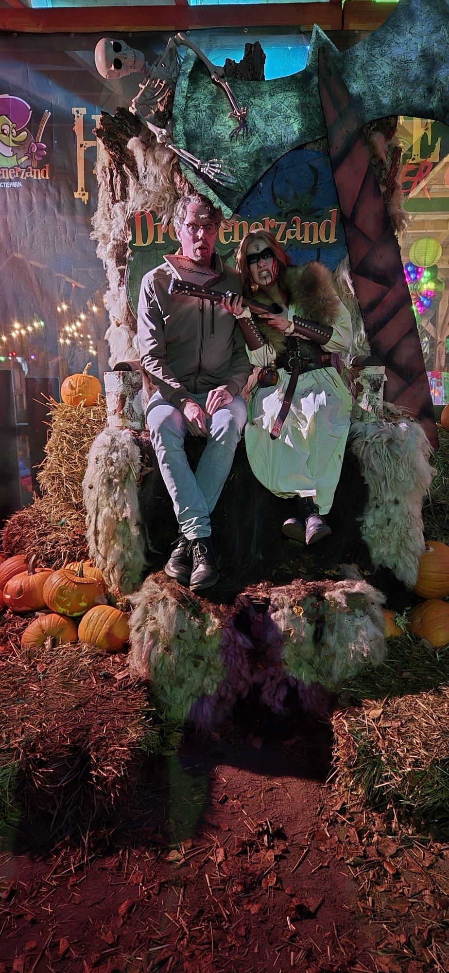 Foto van mij, op een Halloween setting van Drouwenerzand zittend op een grote troon met een gevaarlijk kijkende vrouw met bebloed gezicht die een grote bijl tegen mijn keel houdt.