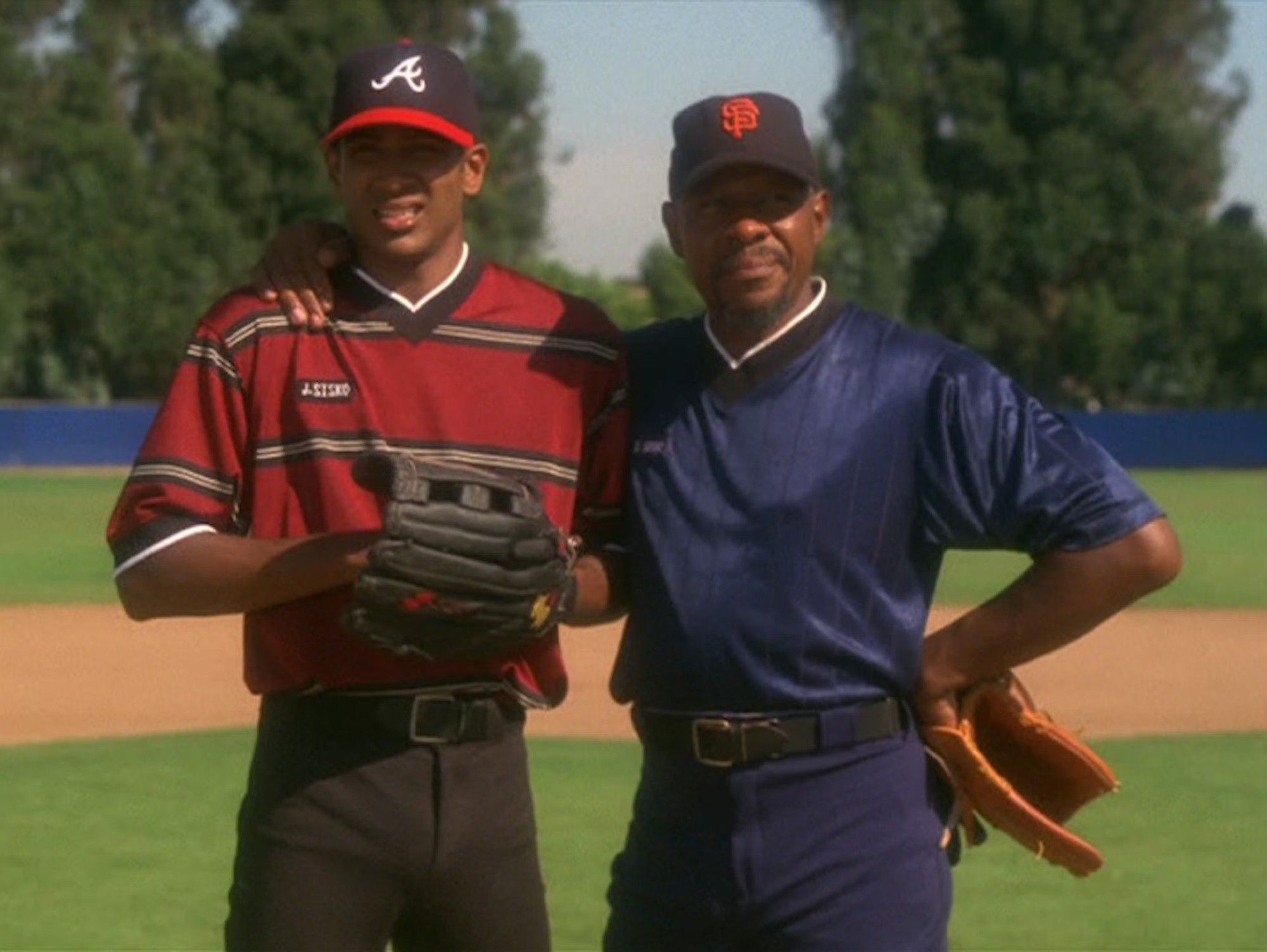 Jake and Ben Sisko from Star Trek DS9 standing on a baseball field. Ben has his arm around Jake, and they both look a little concerned. Jake is wearing a Braves hat, and Ben is wearing a Giants hat.