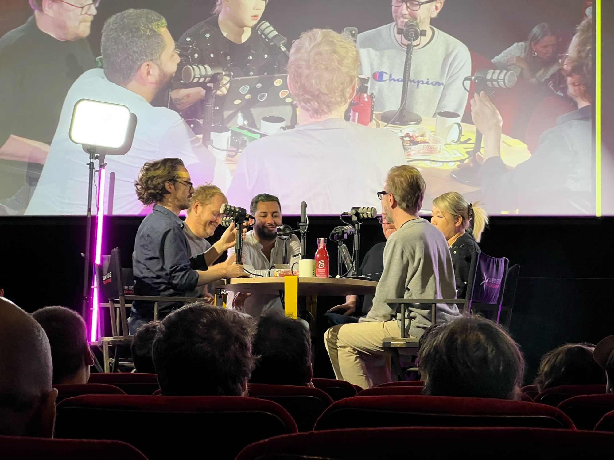 Animateurs et invités installés sur la scène d’un cinéma autour d’une table ronde avec micro pour l’enregistrement d’un live Twitch