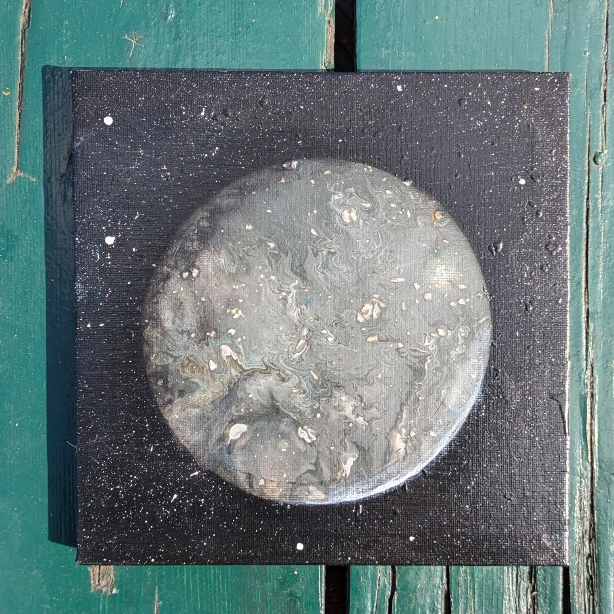 Photo of a painting of a planet with silver, grey, and white colors.