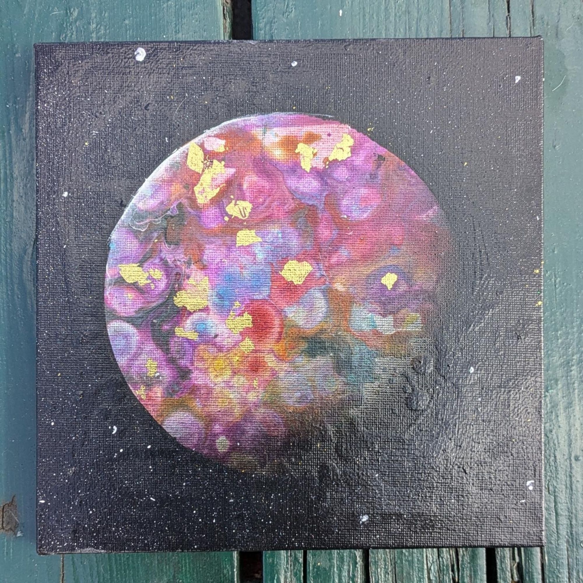 Photo of a painting of a circular object, the exo-moon, with purple, blue, red, orange circles blending together. Gold flecks are scattered across the surface.