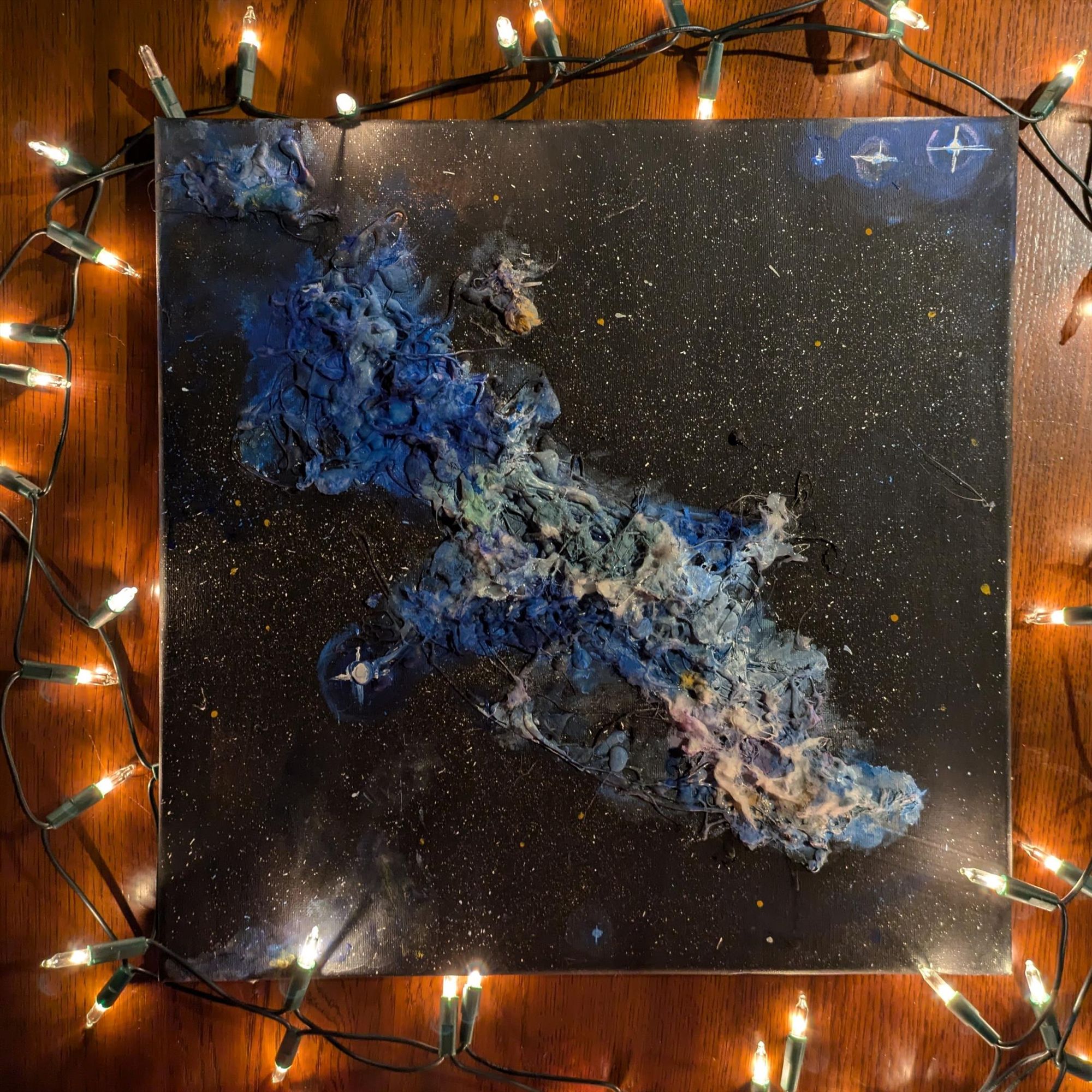 Photo of a square canvas surrounded by fairy lights. On the canvas is the artwork of the witch head nebula. 