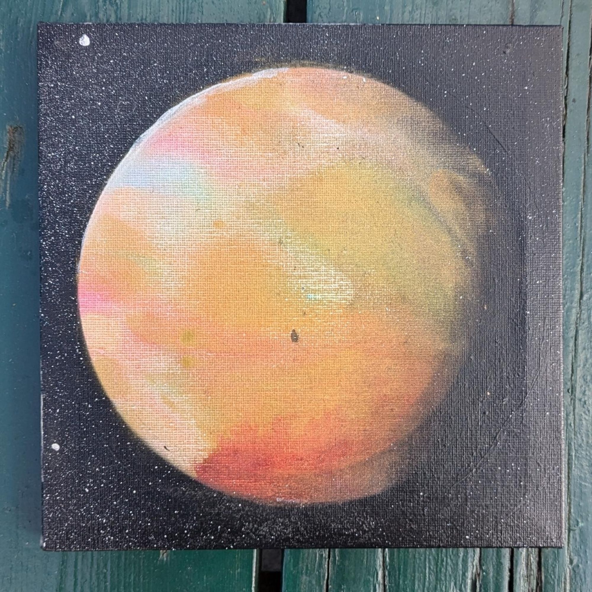 Photo of a painting of a planet with gold, red, white, hues on a square canvas. Stars in the background.