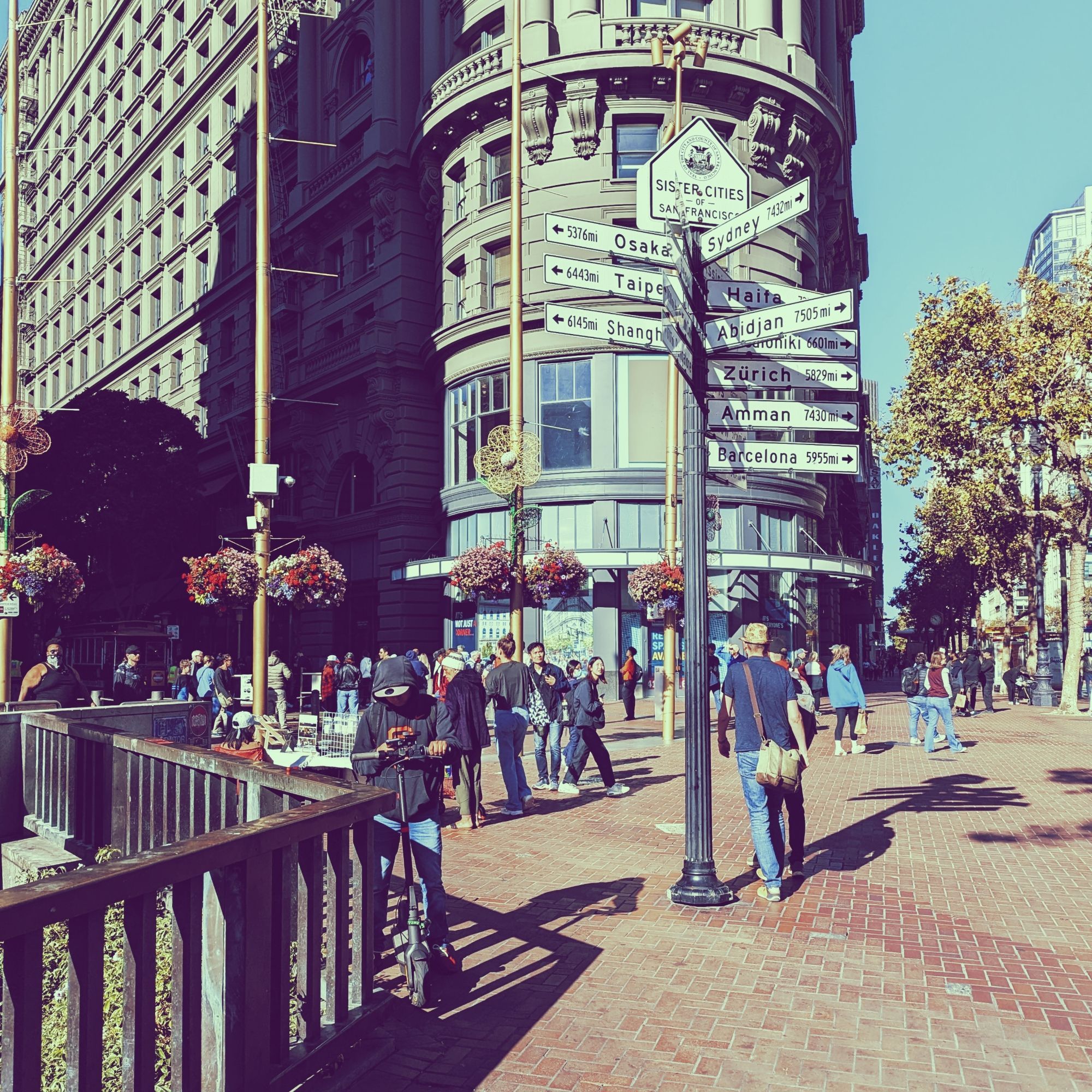 The sister cities sign just outside of the Powell Street subway stop has multiple directions and distances listed for the sister cities of San Francisco, which includes Osaka, Taipei, Shanghai, Sydney, Haifa, Abidjan, Zürich, Amman, and Barcelona.