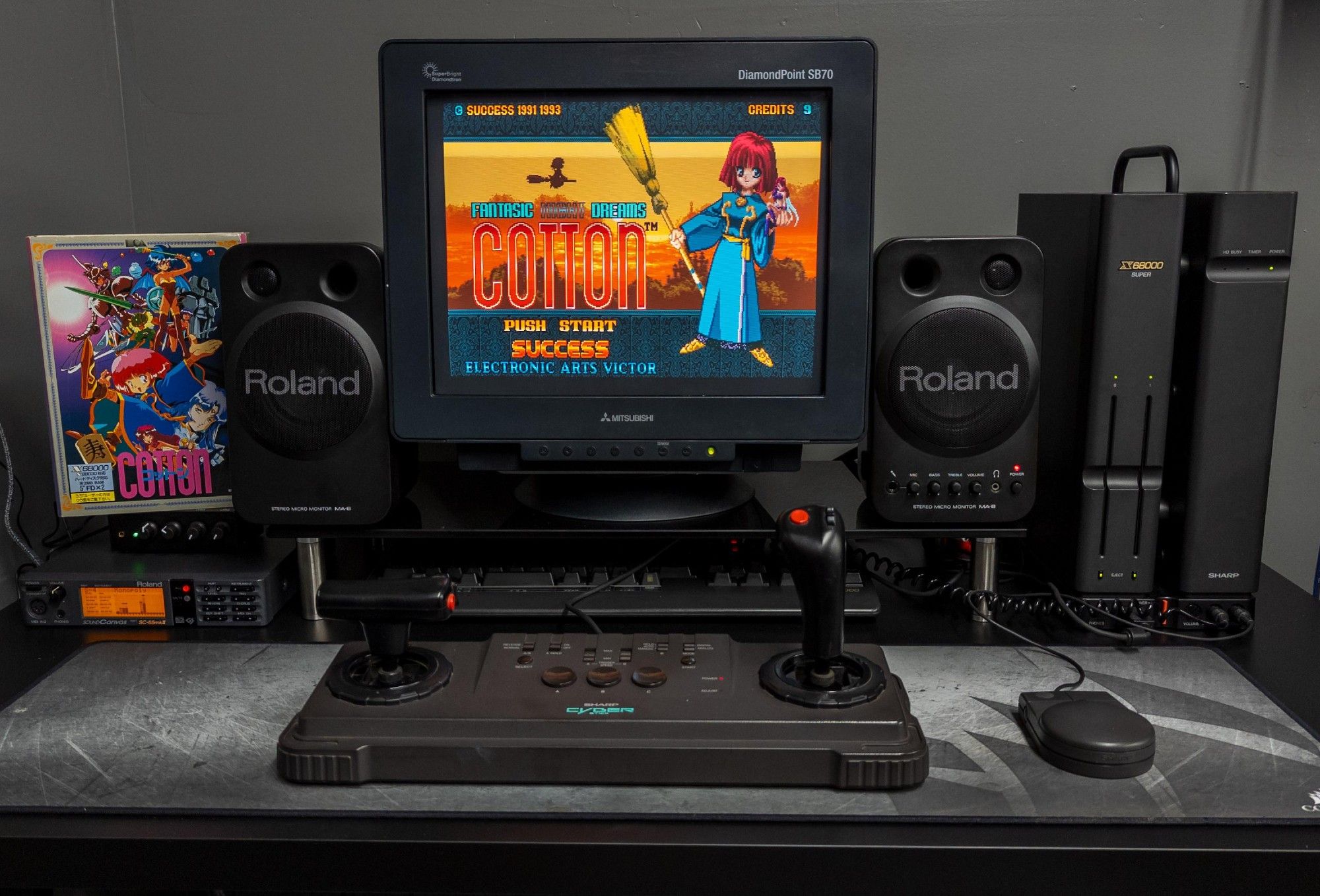 A photo of an incredibly sexy Sharp X68000 setup, all in charcoal grey and black with an MT32 and Roland speakers, and Sharp Cyber Stick throttle and joystick in front of it. Cotton is on the screen.