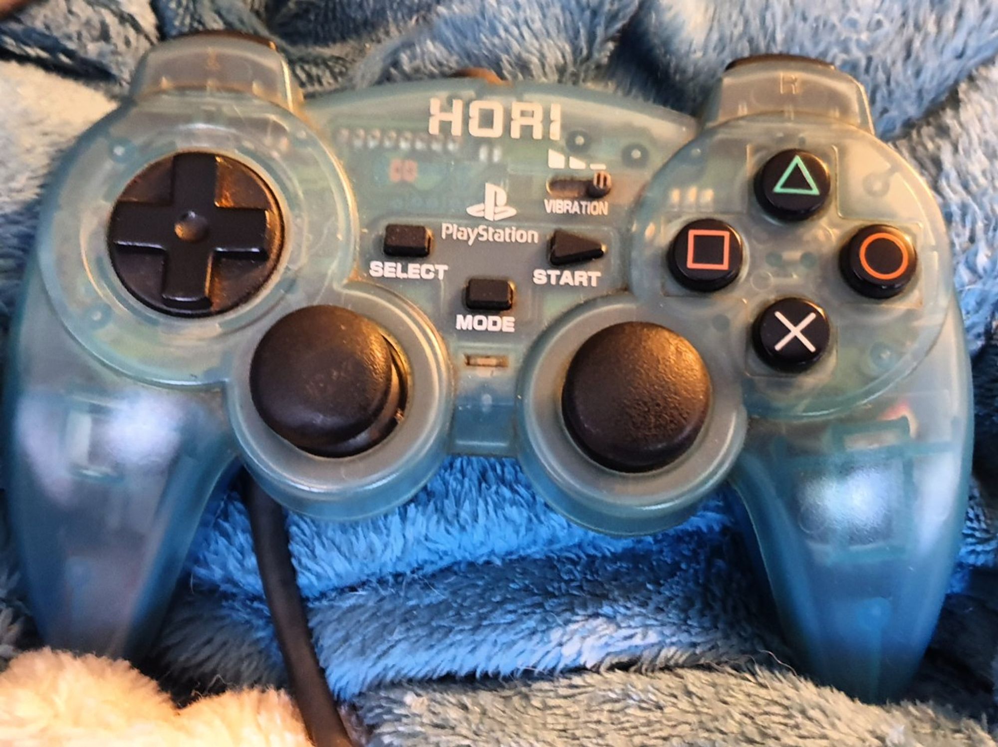 A photo of a Sindou pad. translucent blue with curved grips and a smooth rockerish dpad.