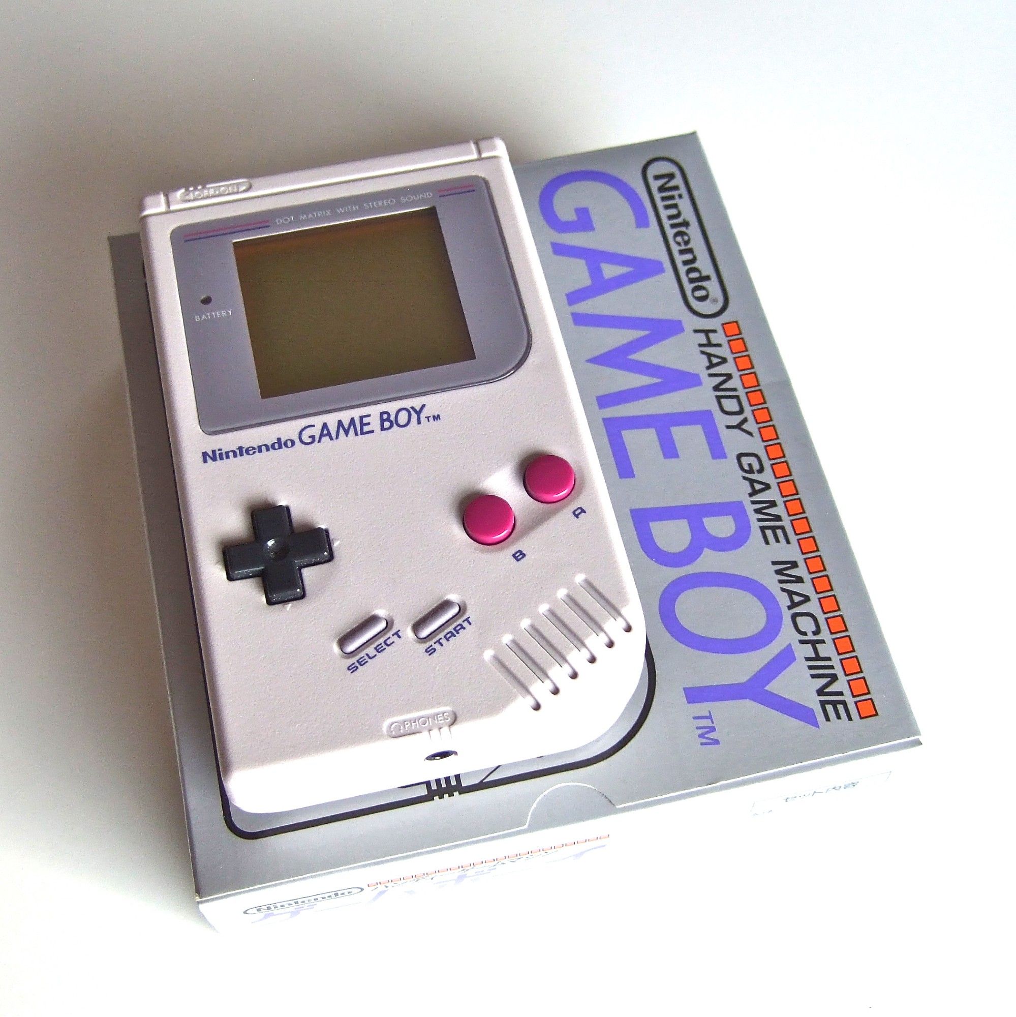 A photo of the Game Boy DMG on top of the snazzy box cover where the line drawing is