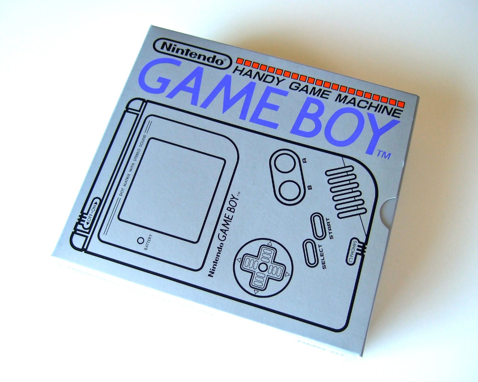 A photo of the Japanese Game Boy box's cover with its simple monochrome line drawing of the Game Boy and Handy Game Machine Game Boy above it.