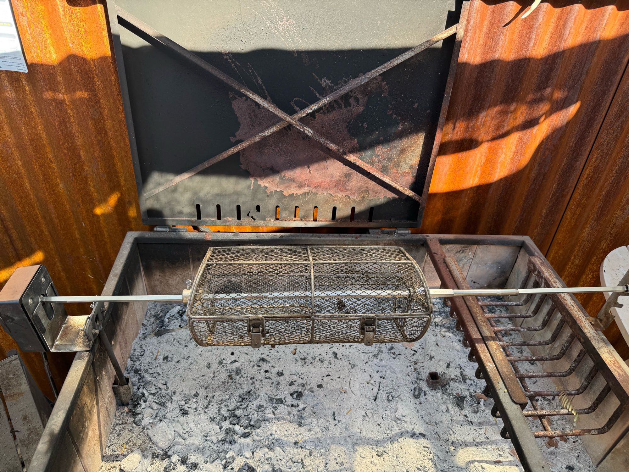 A rotisserie spit over an ashen bed of coals