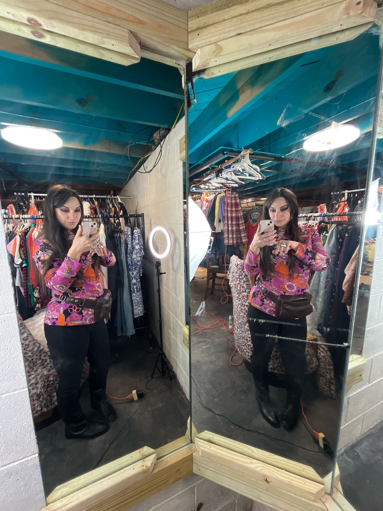 Woman with long straight brown hair and a bright vintage shirt takes a full body selfie in a double mirror.