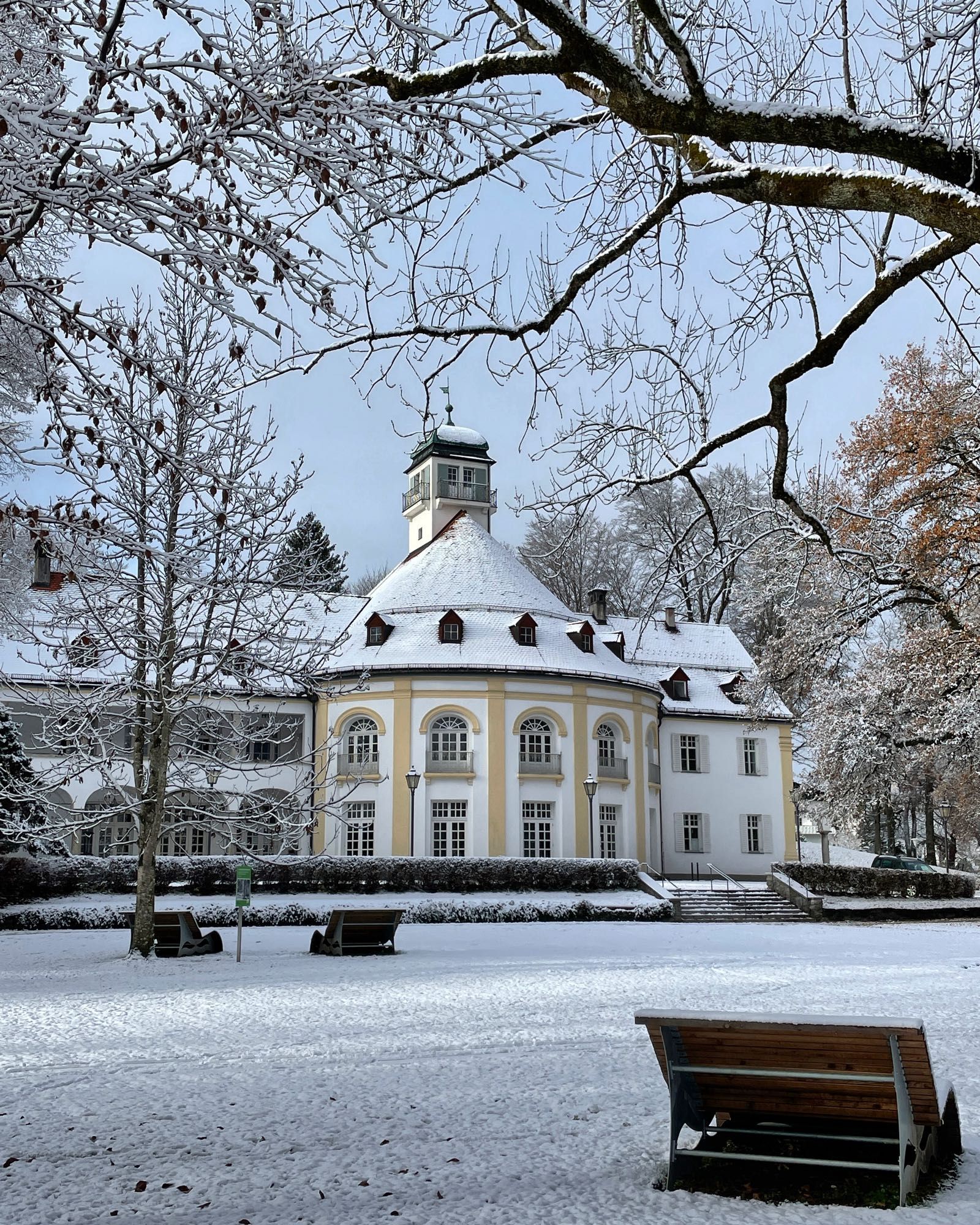 Hauchdünn ist der weiße Schnee im Kurpark mit Blick durch kahle Bäume auf das Kurhaus von Bad Tölz, Oberbayern