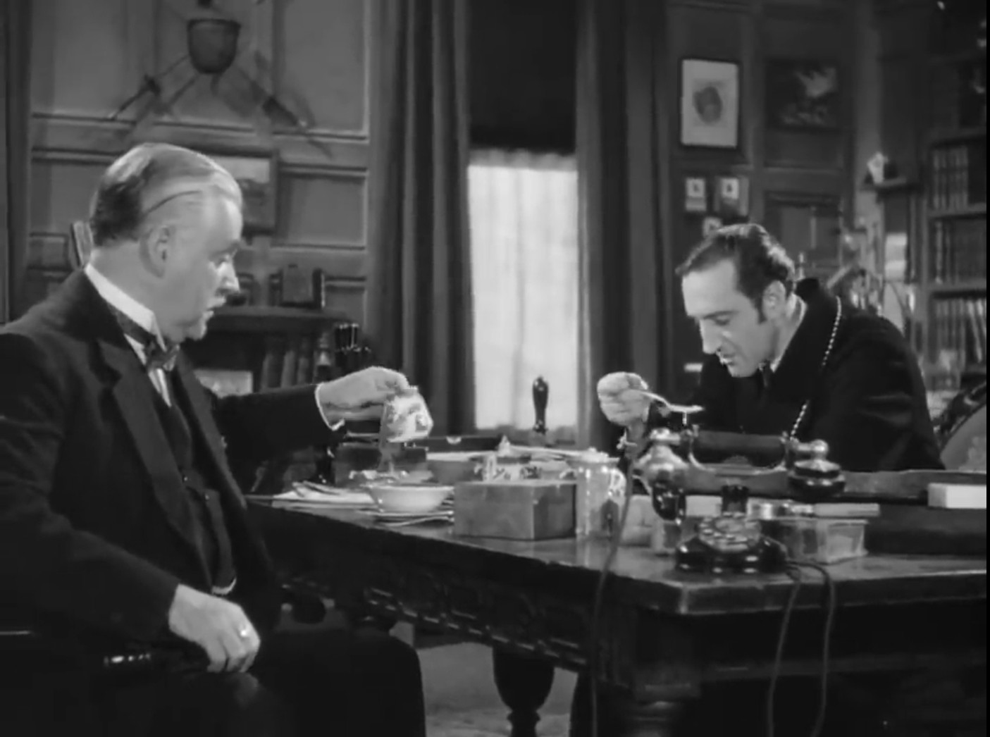 A black-and-white screenshot from 'Sherlock Holmes Faces Death', showing Dr Watson and Sherlock Holmes breakfasting in their 221b Baker Street flat. Watson is delicately pouring cream, while Holmes is hunched possessively over his oatmeal bowl, slurping his food from an overloaded spoon.