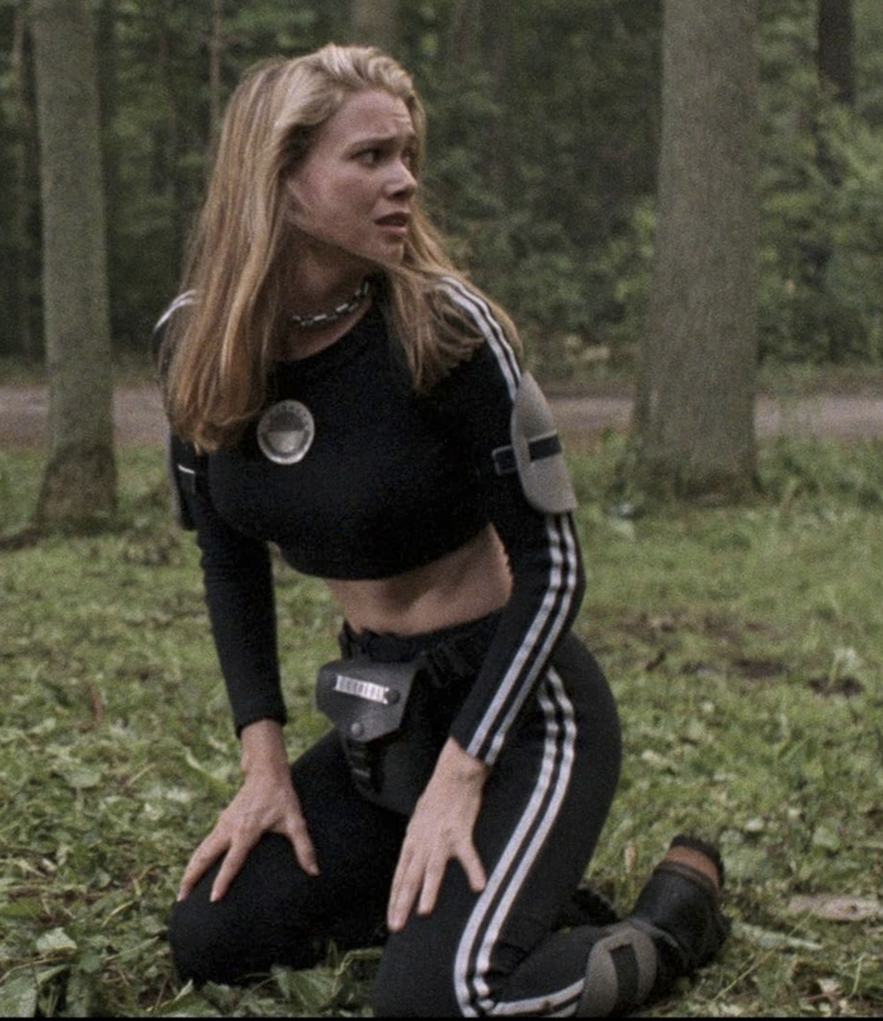 Laurie Holden, a tightly-muscled young blonde woman, in a tight, cropped Adidas tracksuit with 'cool' pads strapped to her arms and ankles and a leather fanny pack.