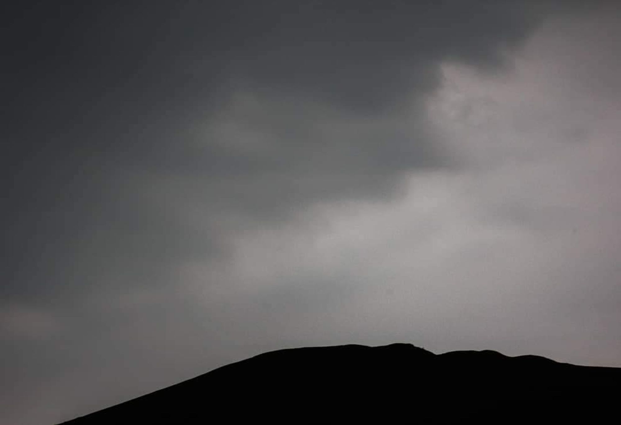 Hillside shrouded in darkness with dark grey and black clouds above at the start of the storm,  just before the rain starts falling