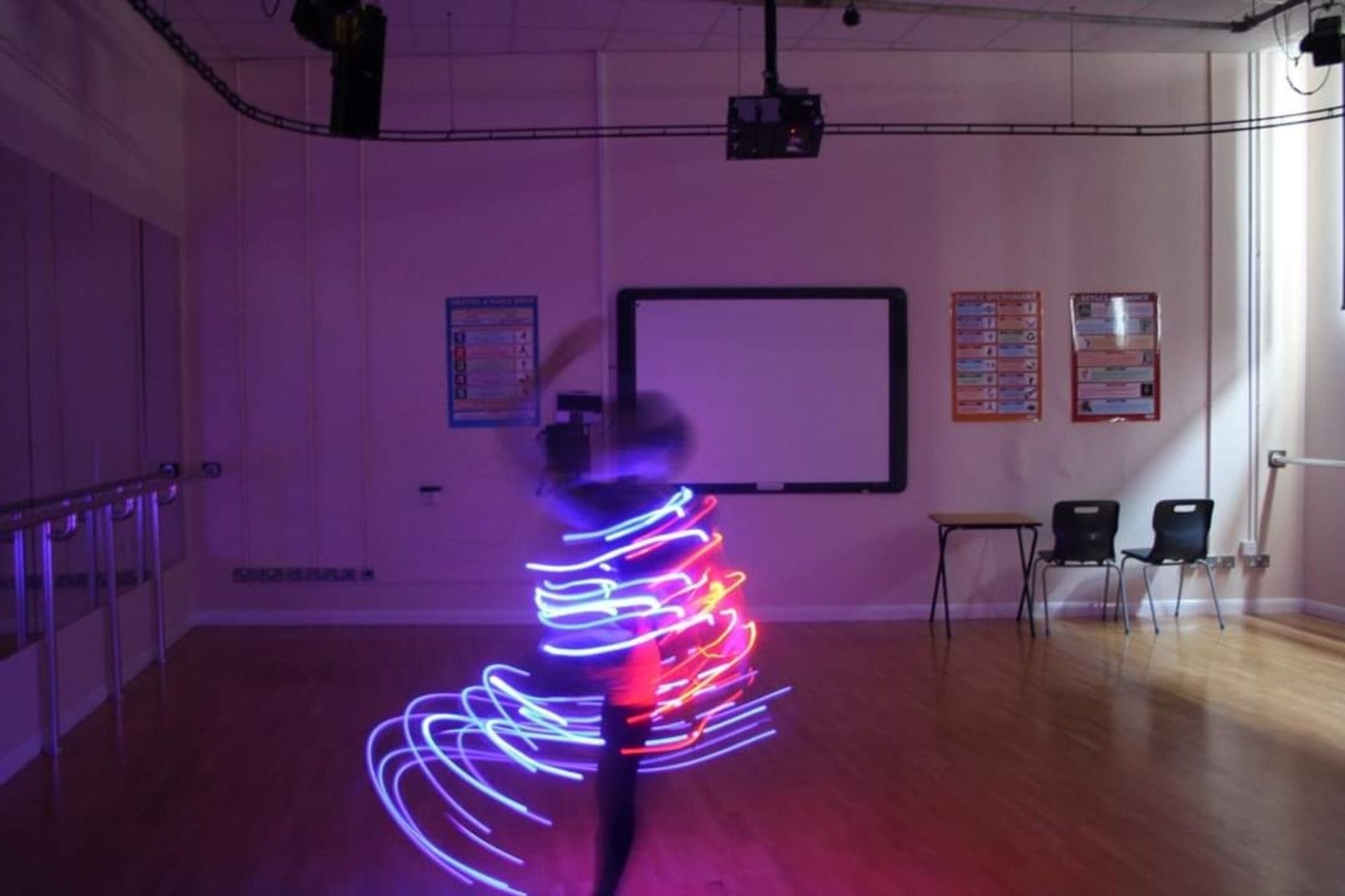 Dancer in a dance studio at college with a balance bar on the left side of the room with a long mirror 
Dancer is spinning around fast with fairy lights on and it has captured the red and blue light trails