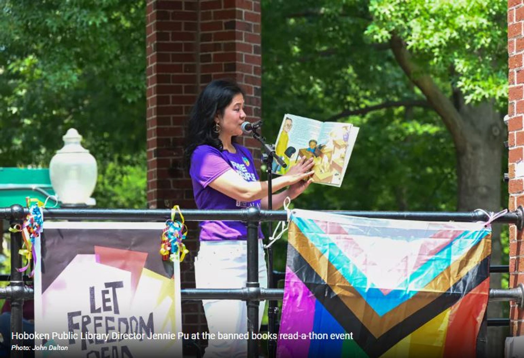 Woman reading a picture book in front of Pride and "Let Freedom Read" flags.
Text on photo: Hoboken Public Library Director Jennie Pu at the banned boos read a thon event. Photo: John Dalton