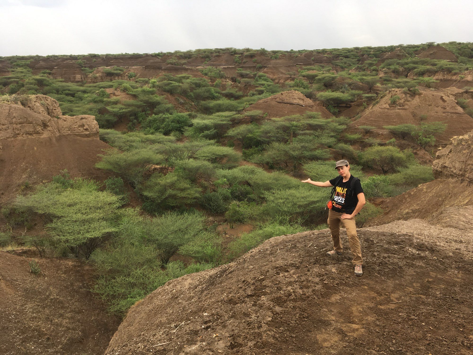 Céline Marie in the field at Kibish, southern Ethiopia. She stands posing on an eroded soft sediment terrace that stands out above lowlands with scrubby vegetation.