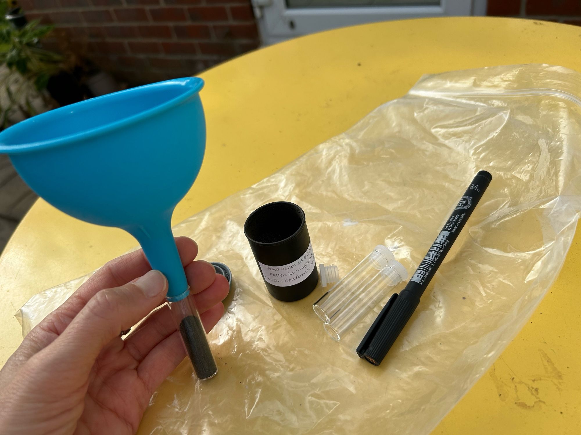 Using a kitchen funnel to decant ash from the film pot to a small glass jar. There’s a marker pen and sample bag also on the table.