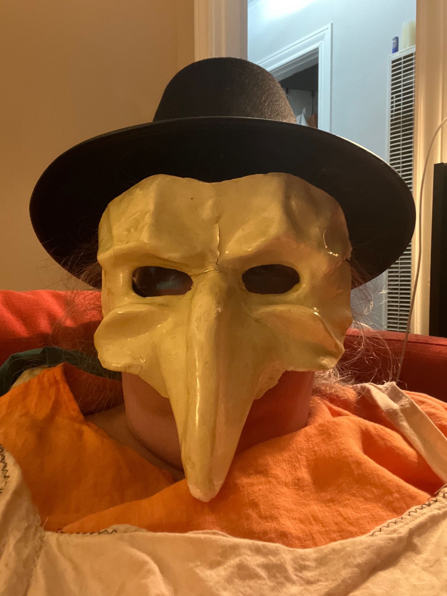 Jenny obscured by a Venetian carnival mask from the 1960s and a cardboard pilgrim hat as she waits for gremlins to knock on the door demanding candy