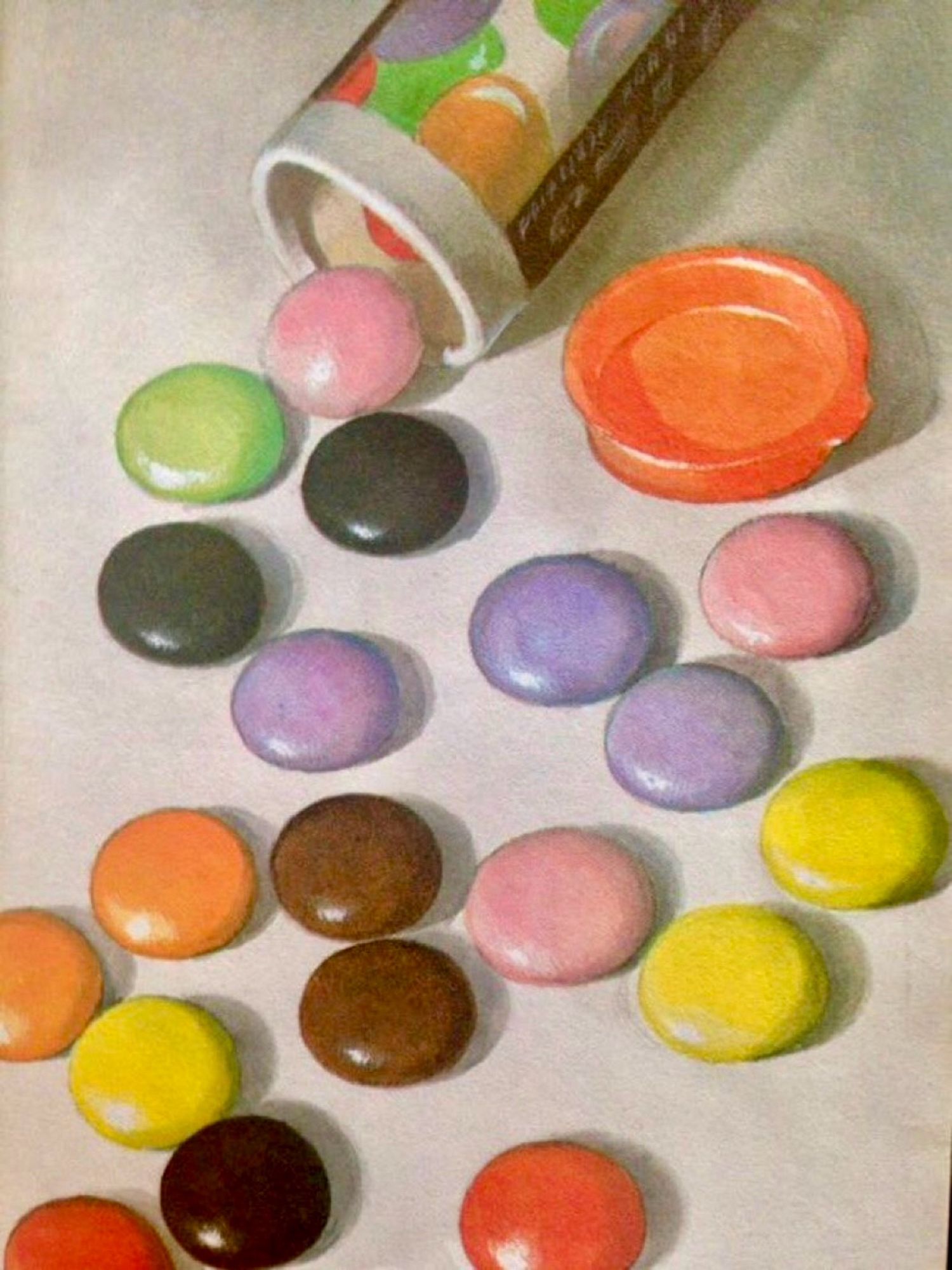 A photo illustration close-up of the end of an open tube of Smarties with a sprinkling of Smarties on a white background