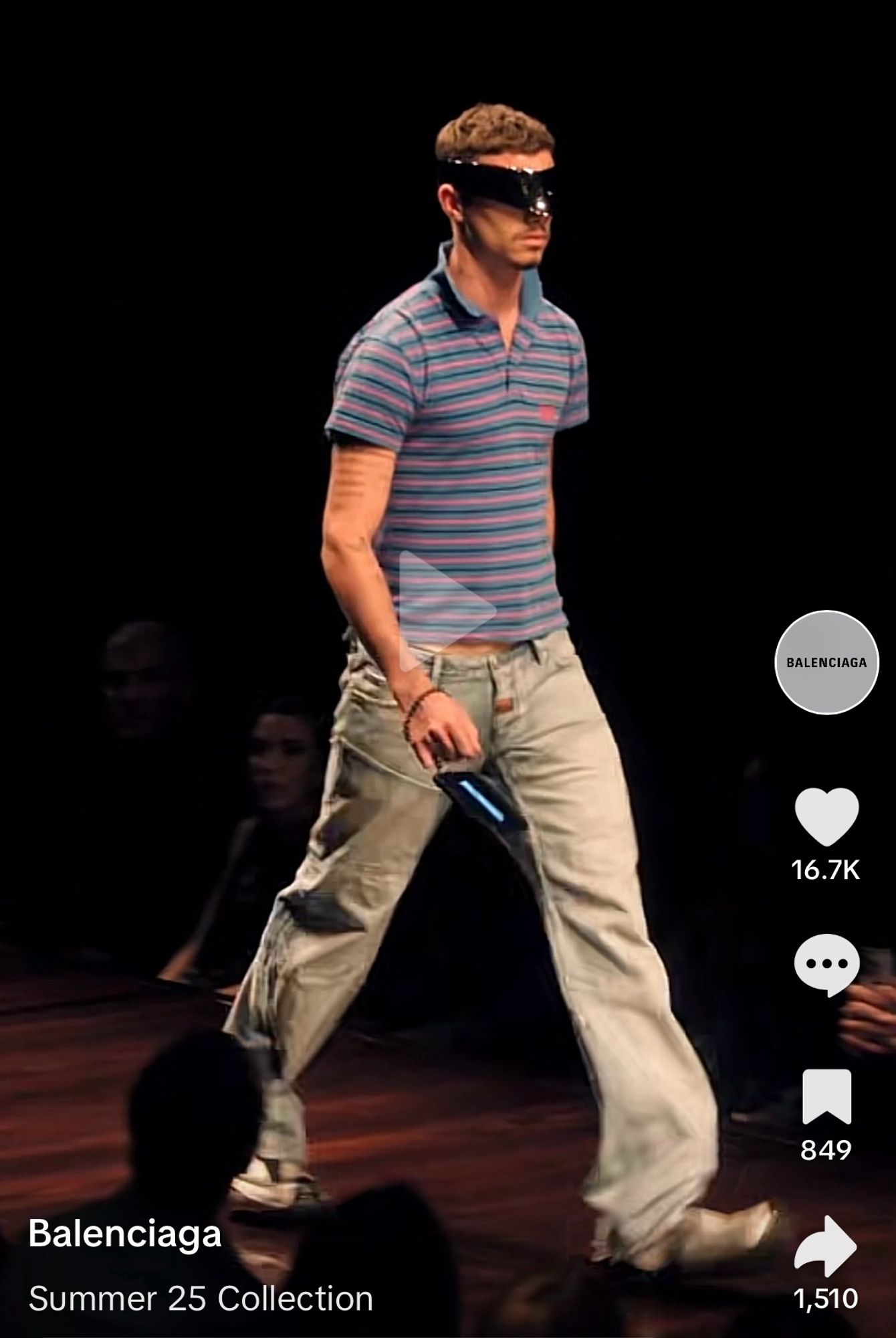 screenshot of the Balenciaga summer 25 collection runway show. male model is wearing light wash baggy work jeans, a too-small polo shirt with popped collar and scuffed oversized sneakers and crazy oversized sunglasses that look like something from science fiction. the shirt is showing some of his middriff