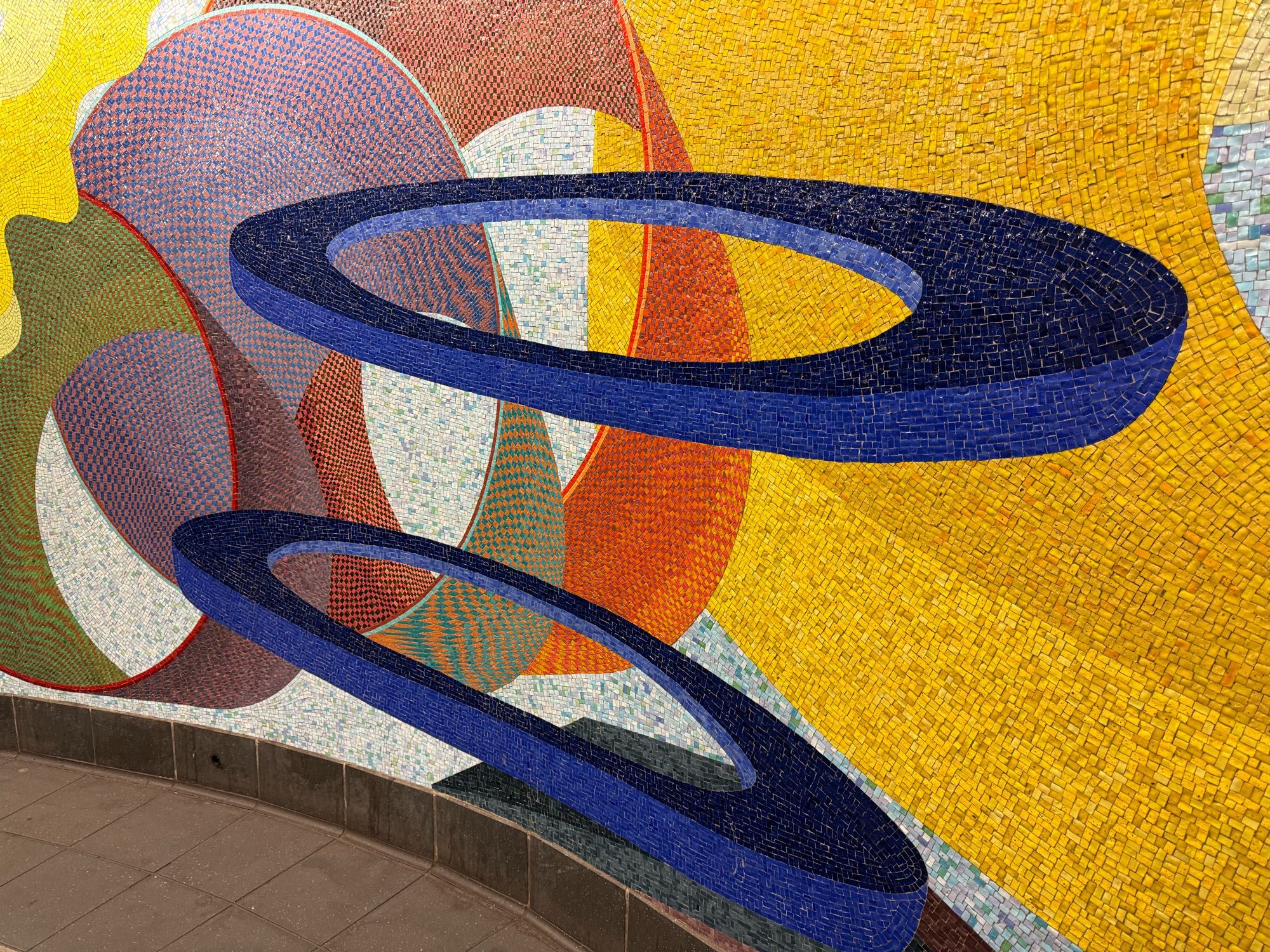 an abstract mosaic of blue discs, orange and multicolored cylinders and a yellow background