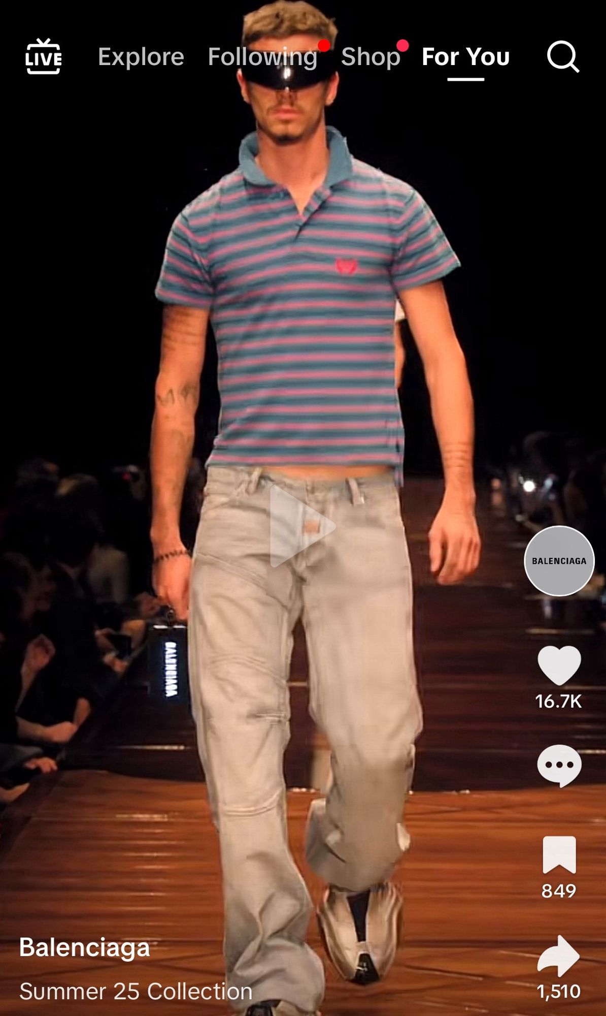 screenshot of the Balenciaga summer 25 collection runway show. male model is wearing light wash baggy work jeans, a too-small polo shirt with popped collar and scuffed oversized sneakers and crazy oversized sunglasses that look like something from science fiction. the shirt is showing some of his middriff