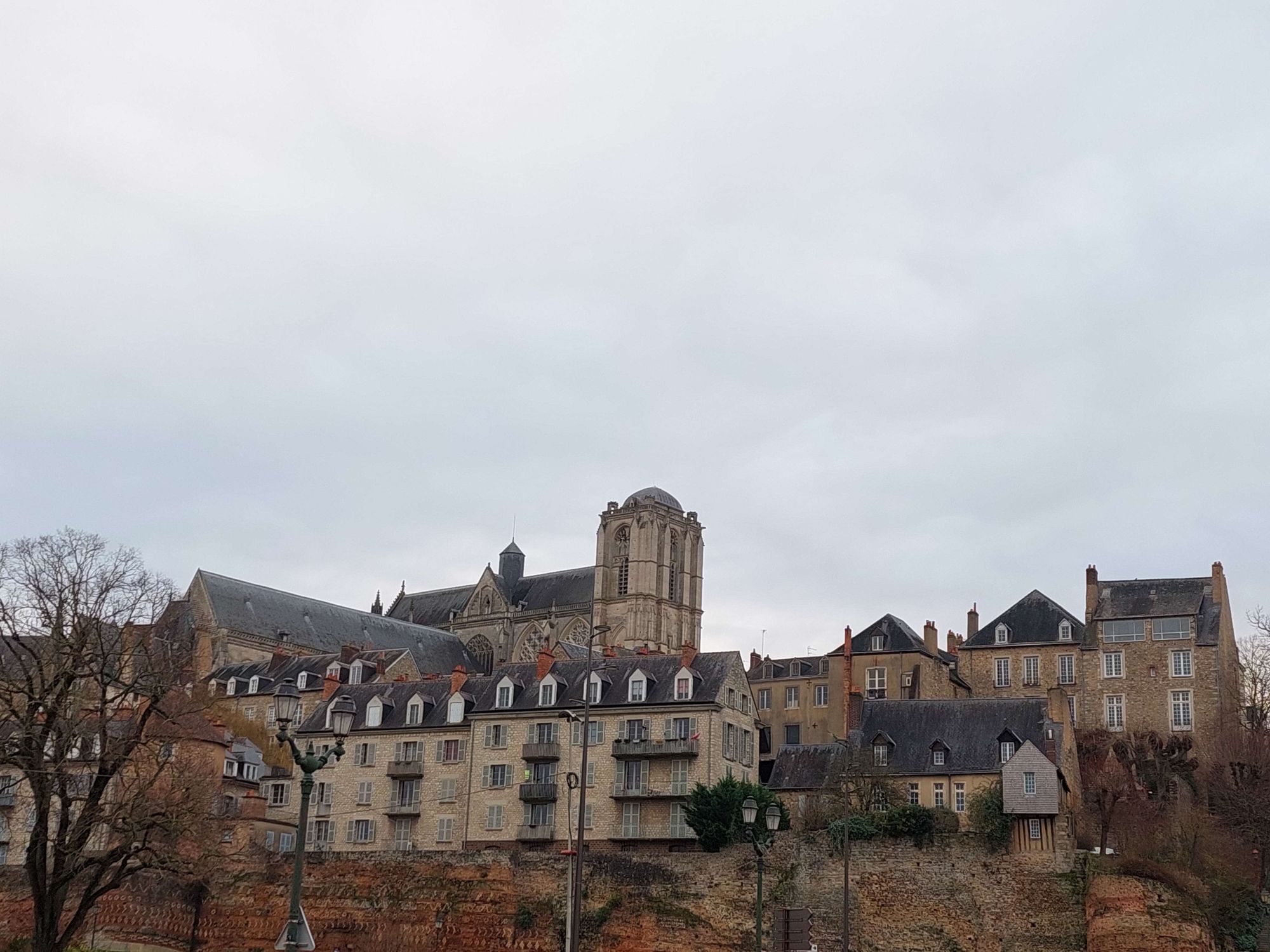 Vue sur la muraille, des habitations et la cathédrale du Vieux-Mans. Le ciel est gris et nuageux.