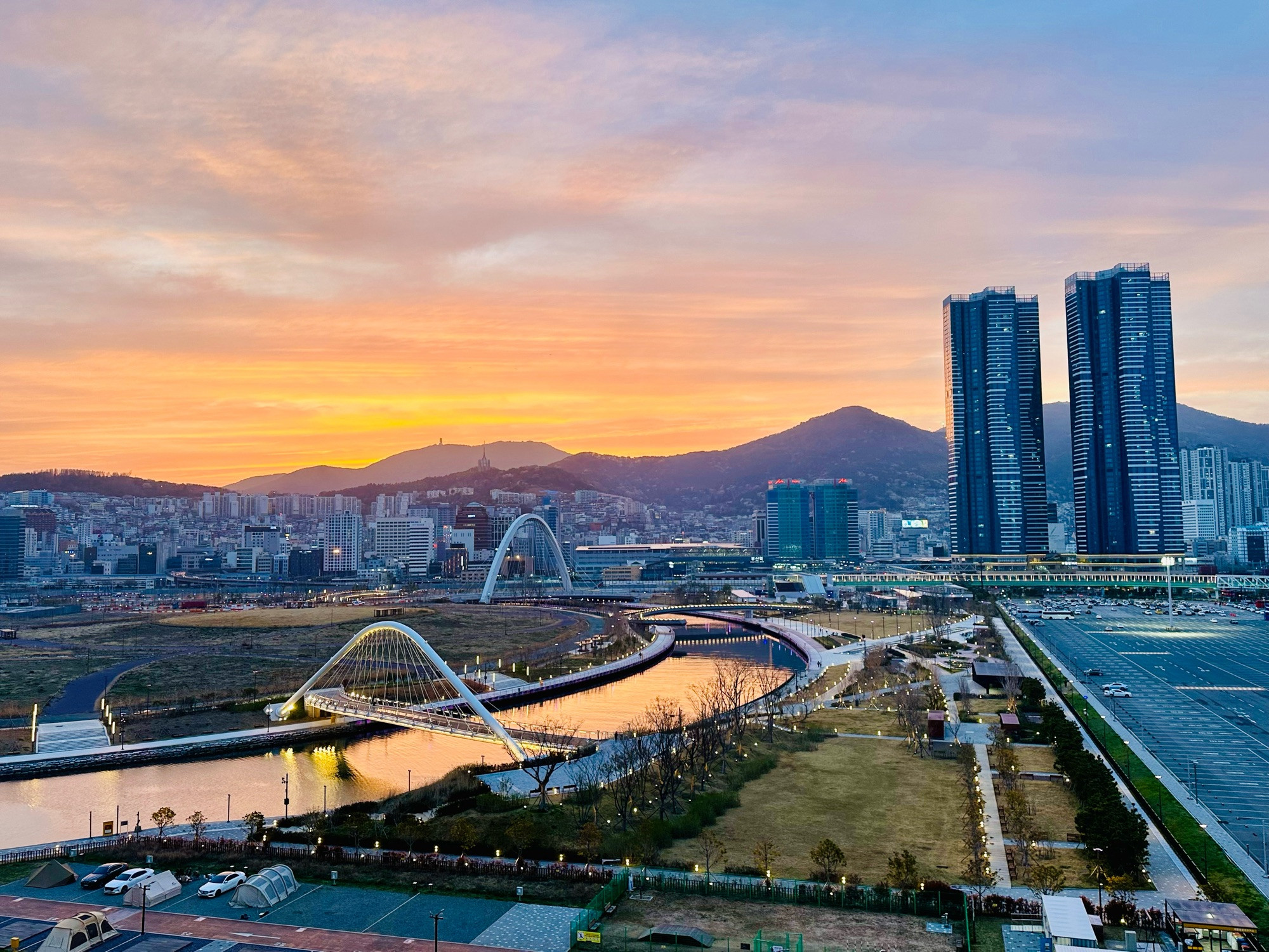 An orange sunset in Busan, South Korea, taken from the Port of Busan facing a river and two arch bridges