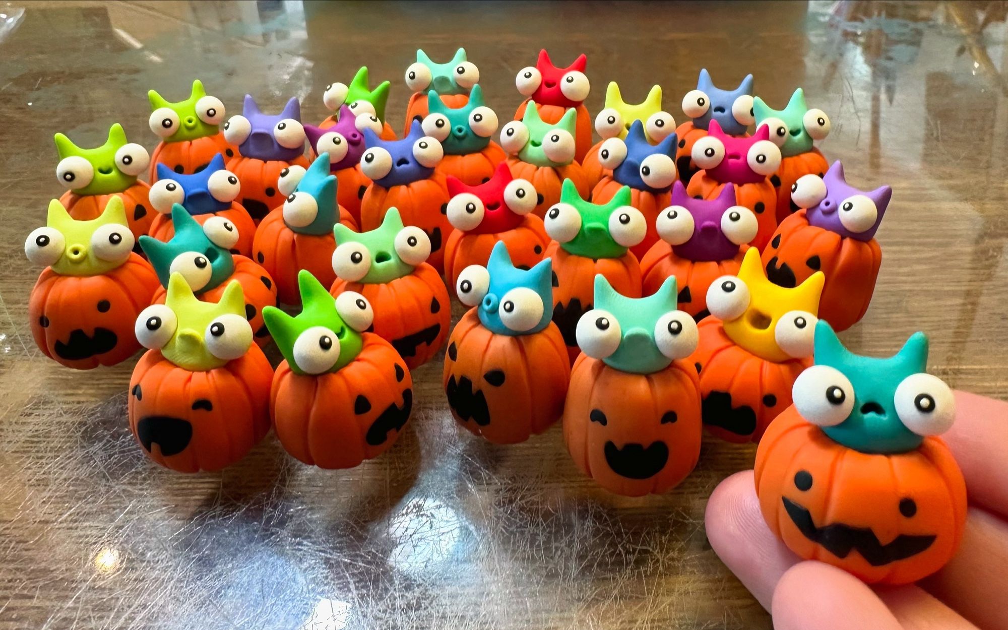 A whole bunch of tiny sculpted jack-o-lanterns with colorful little creatures popping out the top. One is held in a hand.