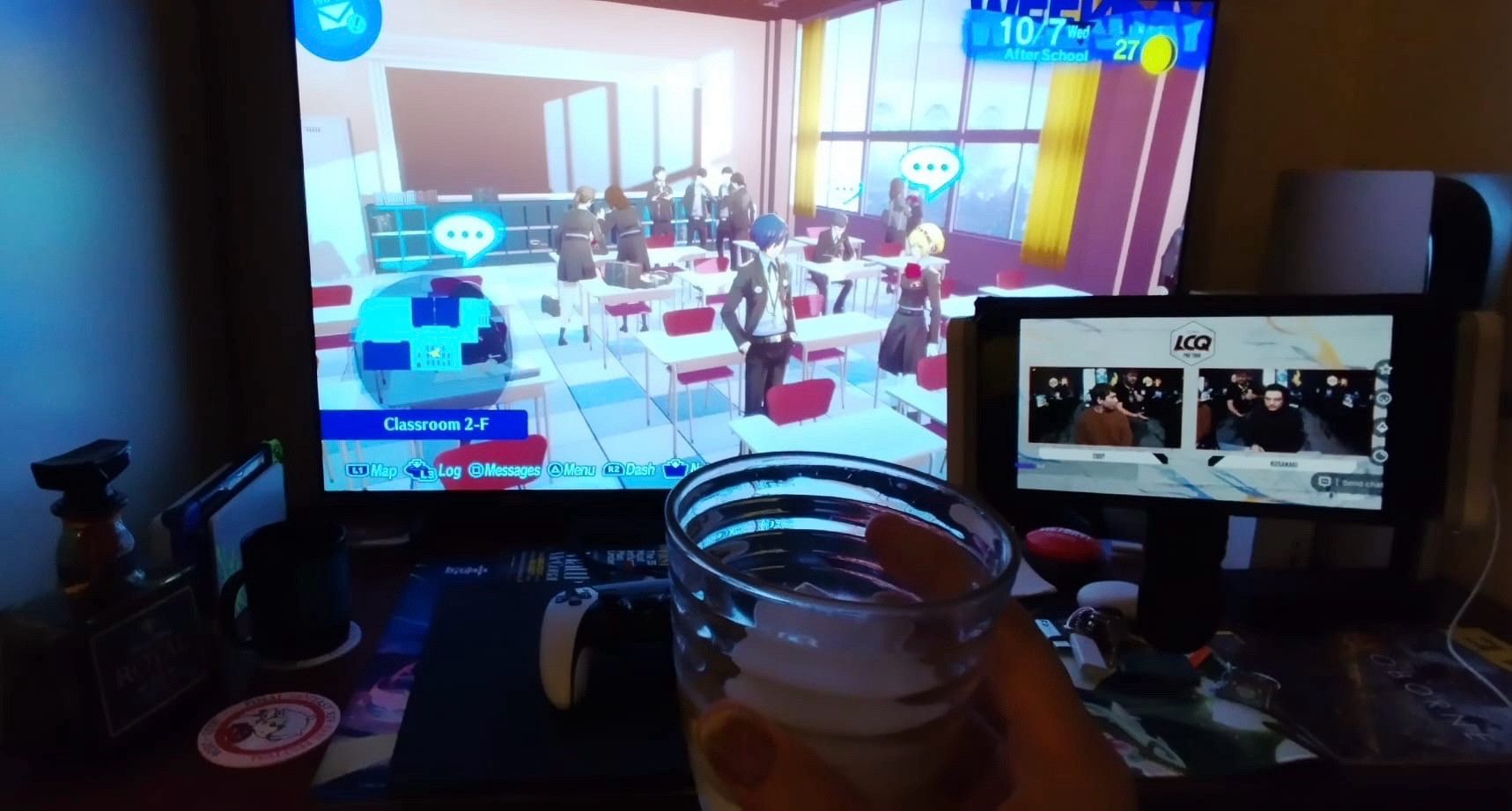 First person view holding up a glass of Japanese whiskey on the rocks in front of a TV with Persona 3 Reload while a phone screen is streaming Capcom Cup last chance qualifier