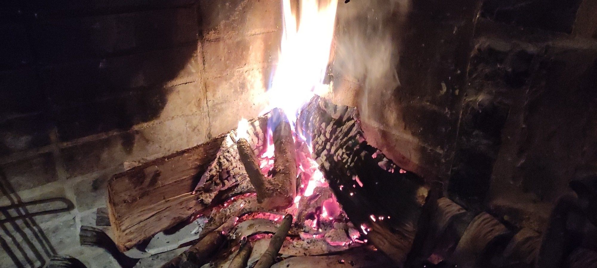 Fireplace with tree logs on fire because outside we are going to winter temperatures.
There's an iron support in order to get air from below and set a more vigorous fire with two dragon heads at the front.