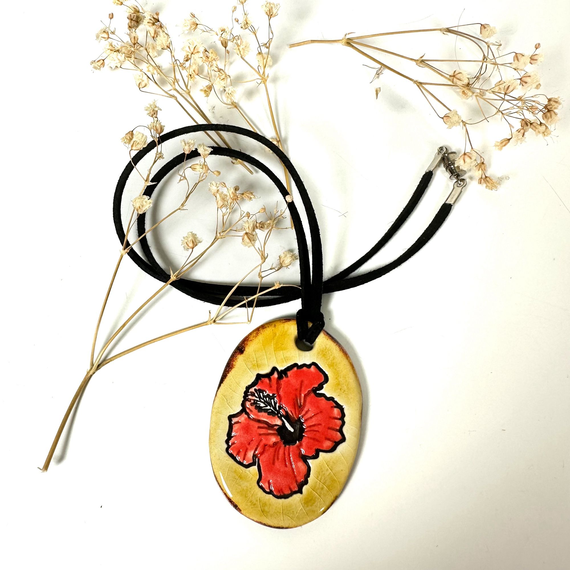 A handmade ceramic pendant with a hibiscus flower design on in made by surlyramics