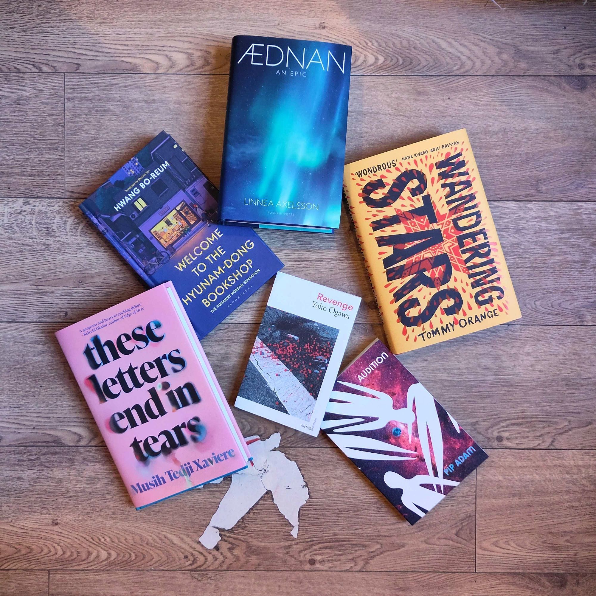 Six books face-up on a wooden floor: Welcome to the Hyunam Dong Bookshop, Aednan, Wandering Stars, Audition, Revenge and These letters end in Tears